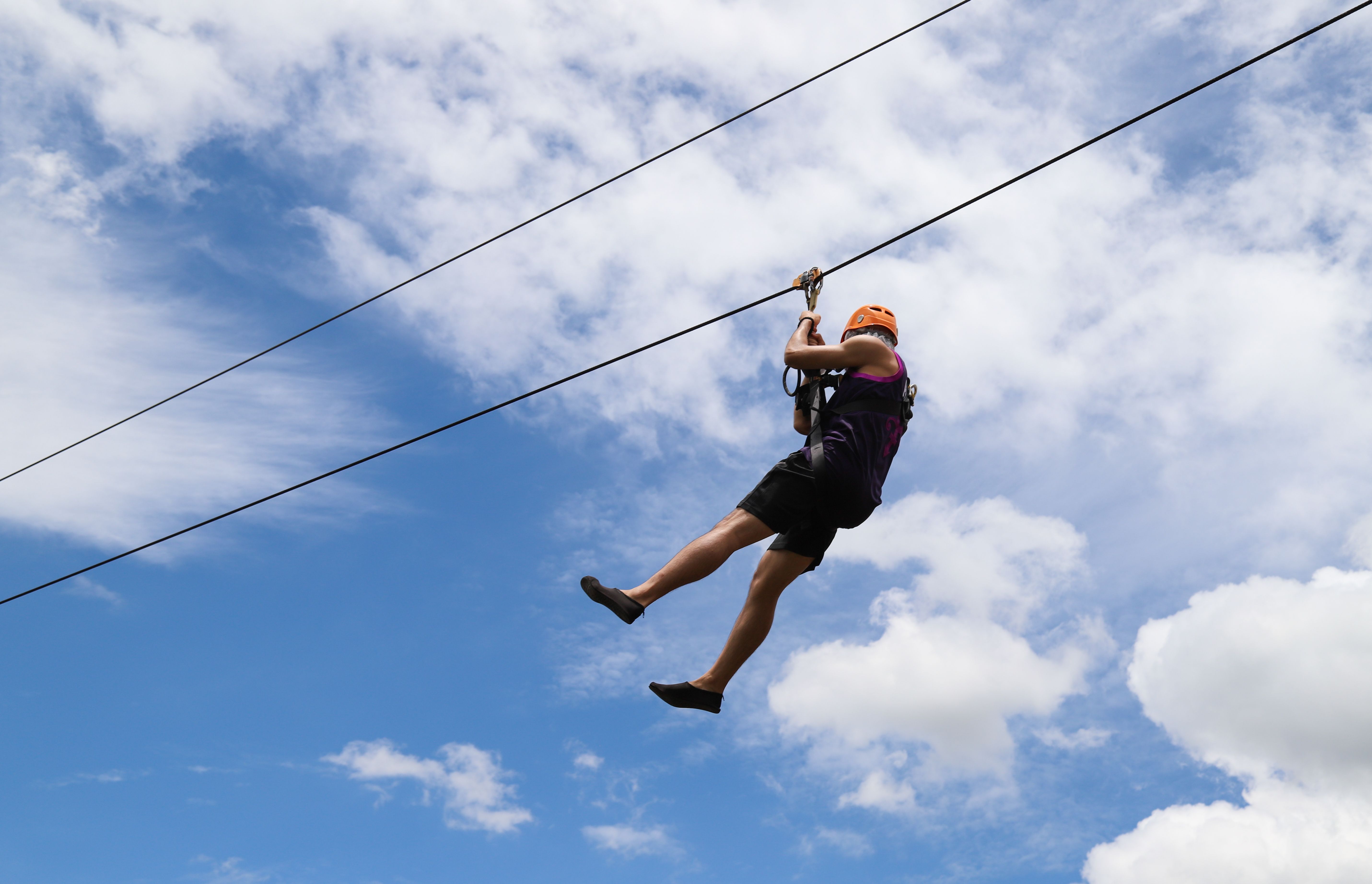 Closeup of a man gliding on trolley zipline in adventure park with cloudy blue sky