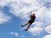 Closeup of a man gliding on trolley zipline in adventure park with cloudy blue sky