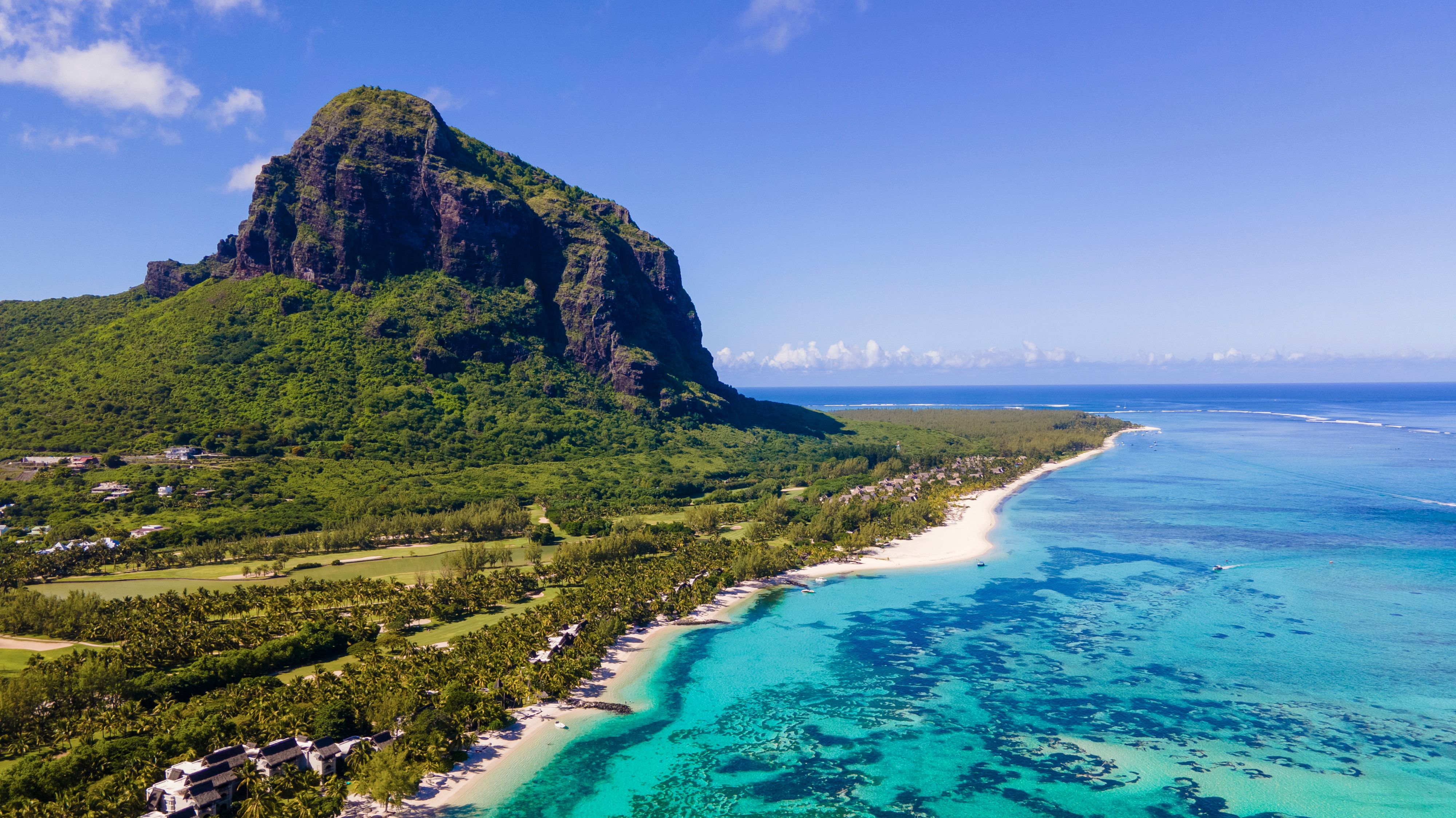An aerial view of the Le Morne mountain with palm trees, white sand and a clear blue ocean stretching out from the base 