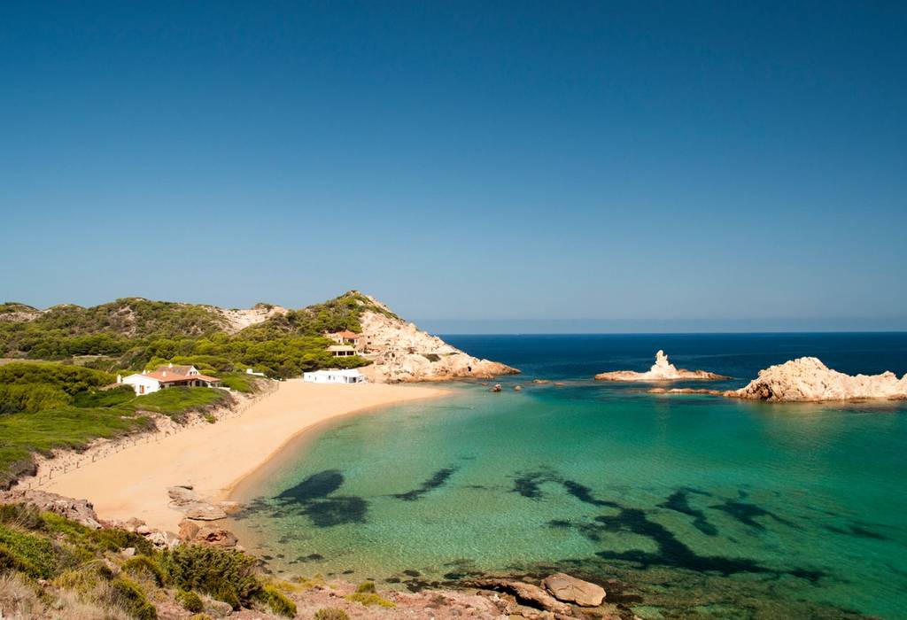 A view of Cala Pregonda beach in Menorca, Balearic Islands backed by grass covered sand dunes and clear blue sea