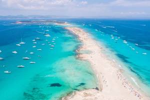 An aerial view showing many yachts anchored off the coast of Formentera Ibiza, with turquoise Mediterranean Sea and ocean blue water