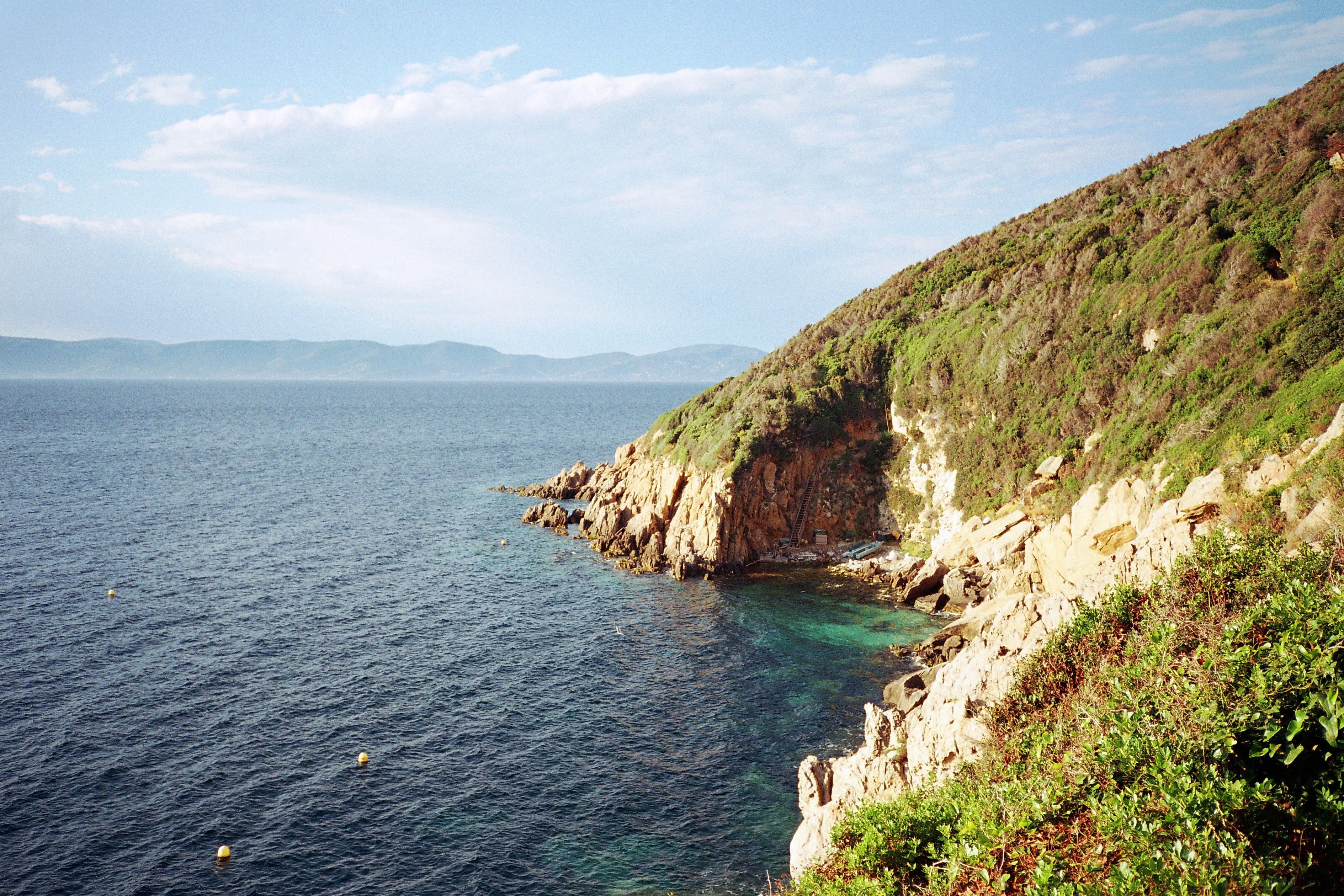 View of a rocky, shrub-covered coastline in the Mediterranean on a sunny day.