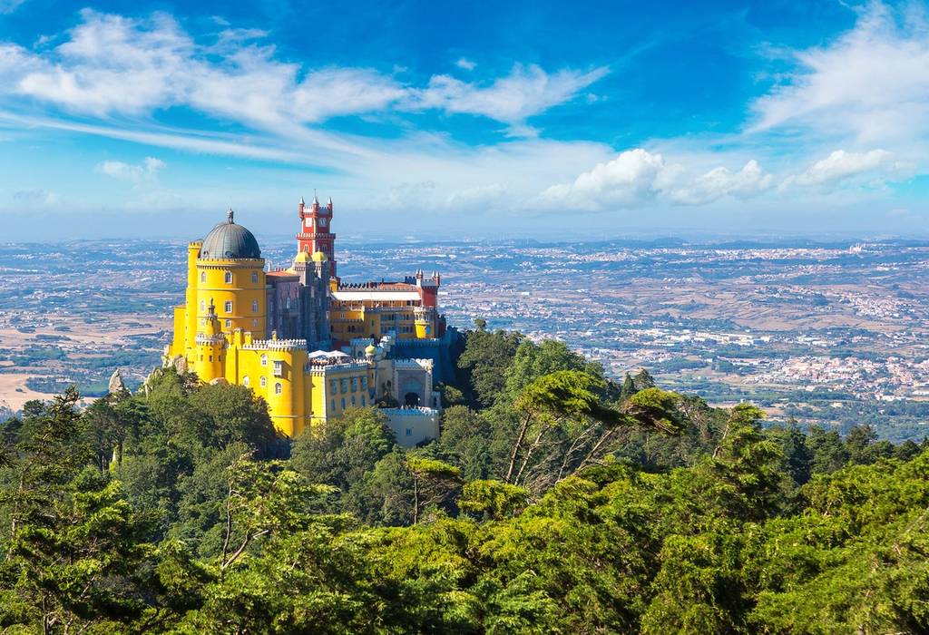 A bright yellow and red castle rises up from a tree-covered hill and overlooks Portuguese countryside