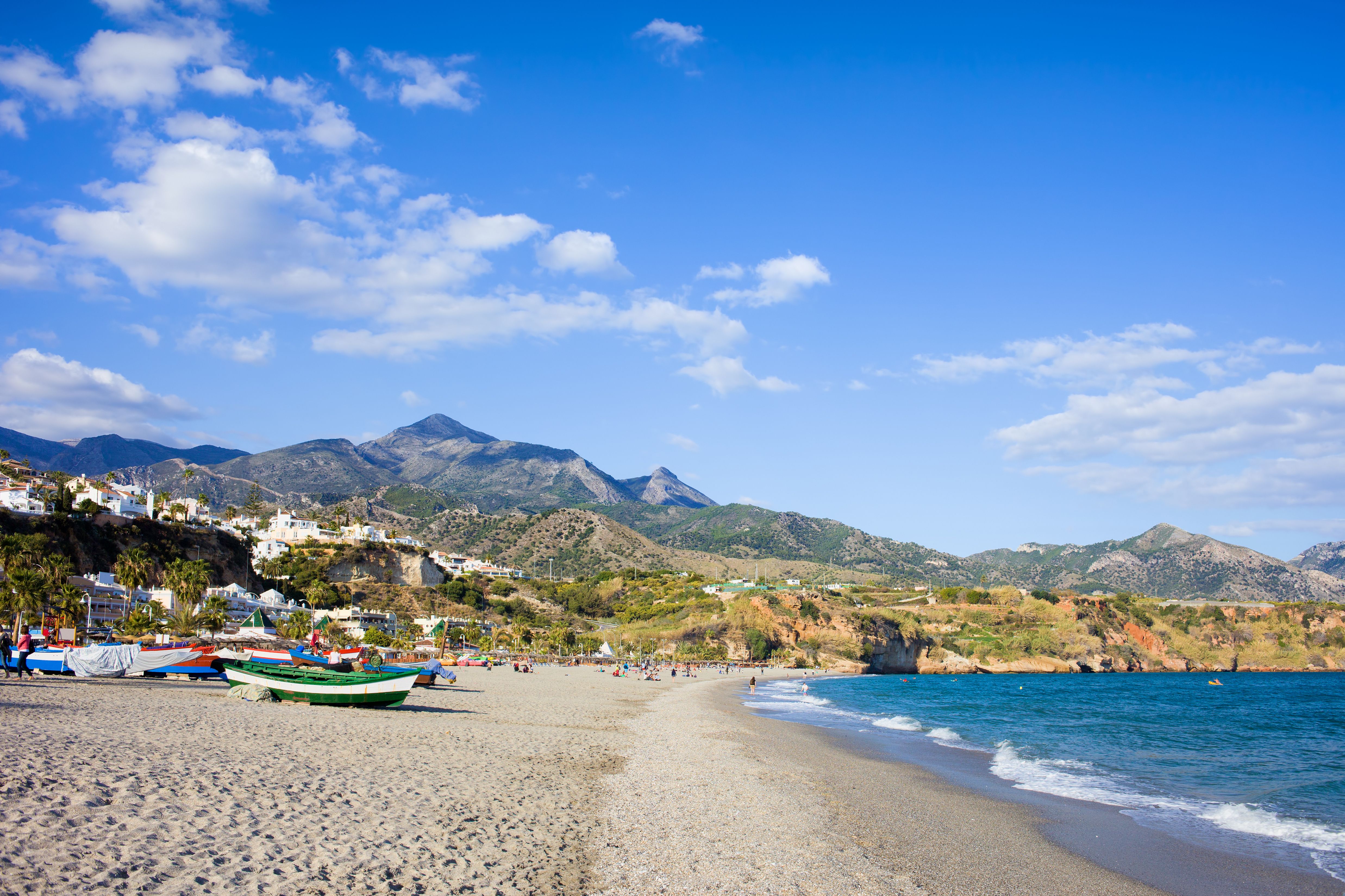 View of boats and kayaks on the soft sand Burriana Beach with mountains in the background