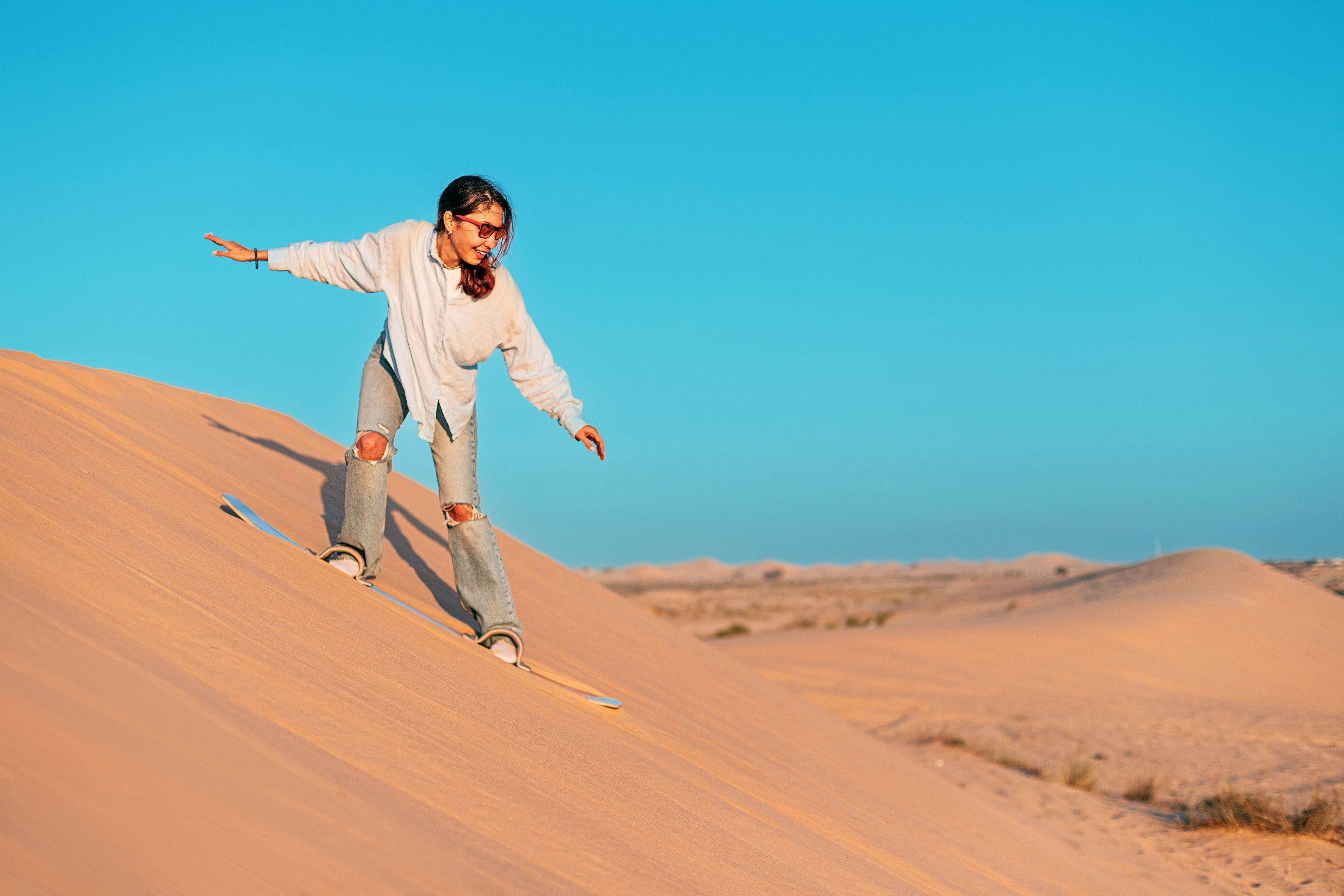 Young woman sand boarding down a sandy dune in the desert