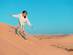 Young woman sand boarding down a sandy dune in the desert