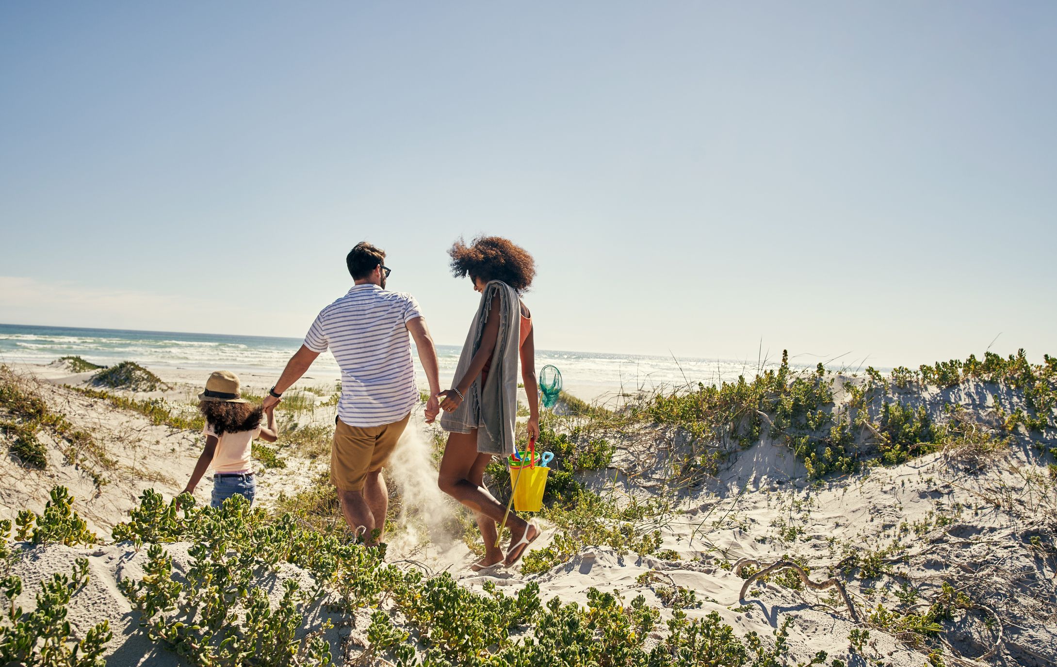 A view of a little girl and her parents walking along a beack with a bucket and spade