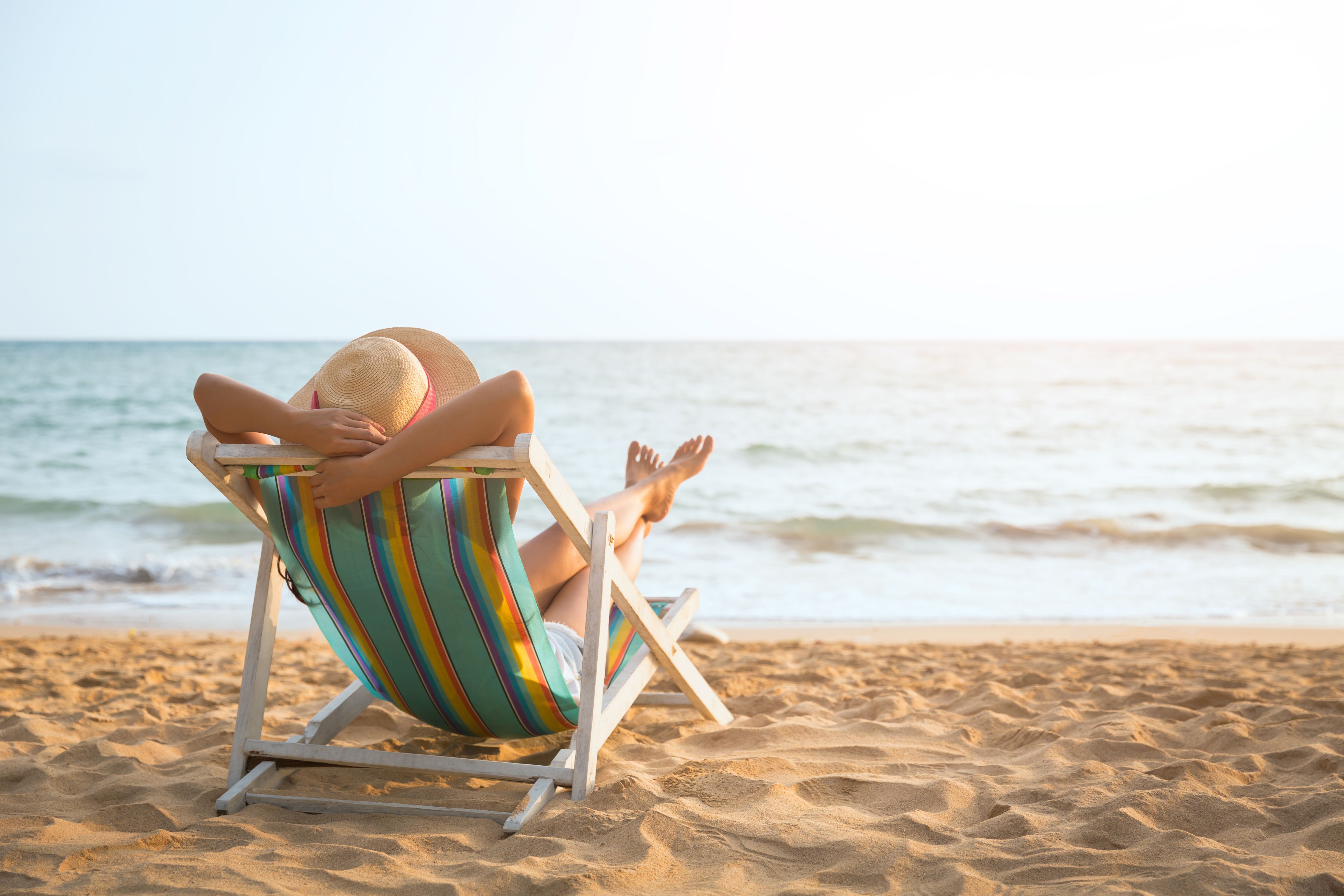 A back view of a woman lounging on a deckchair on a beach looking out to sea