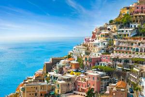 Colourful pink, yellow and orange houses spill down the hillside of Positano with the calm Mediterranean in the background