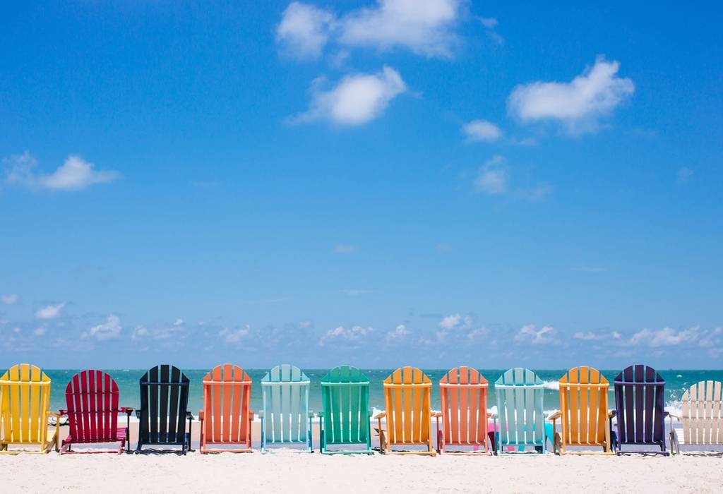 A row of colourful sun-loungers facing the sea on a white-sand beach