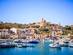 A harbour front view of the island of Gozo in Malta with buildings set into the hillside and colourful boats moored in the harbour