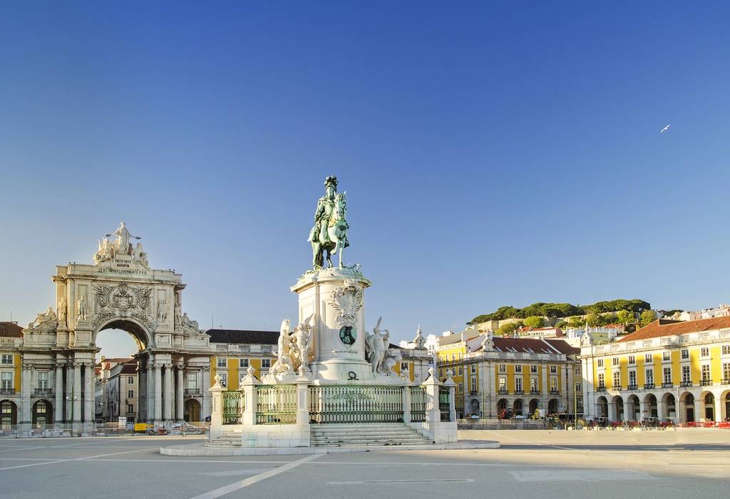 A view of the empty Praca do Comercio square as the sun rises with the ornate Rua Augusta triumphal arch on the left and the statue of King Joseph in the centre