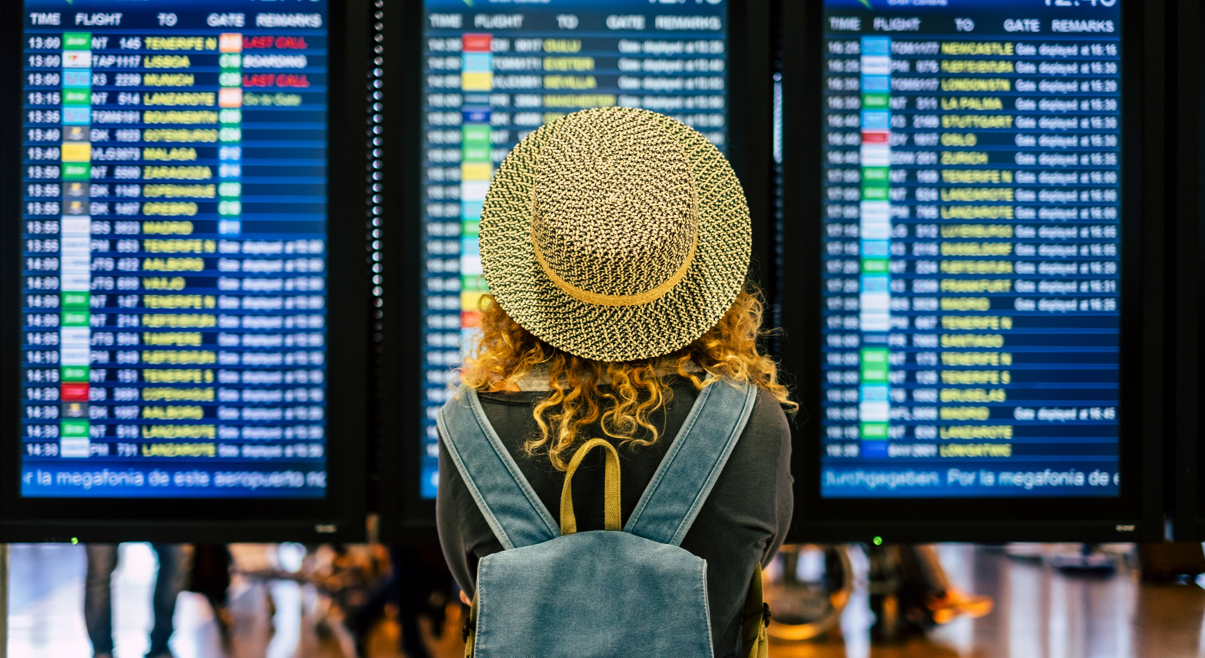 The back of a woman looking up at a departure board in an airport