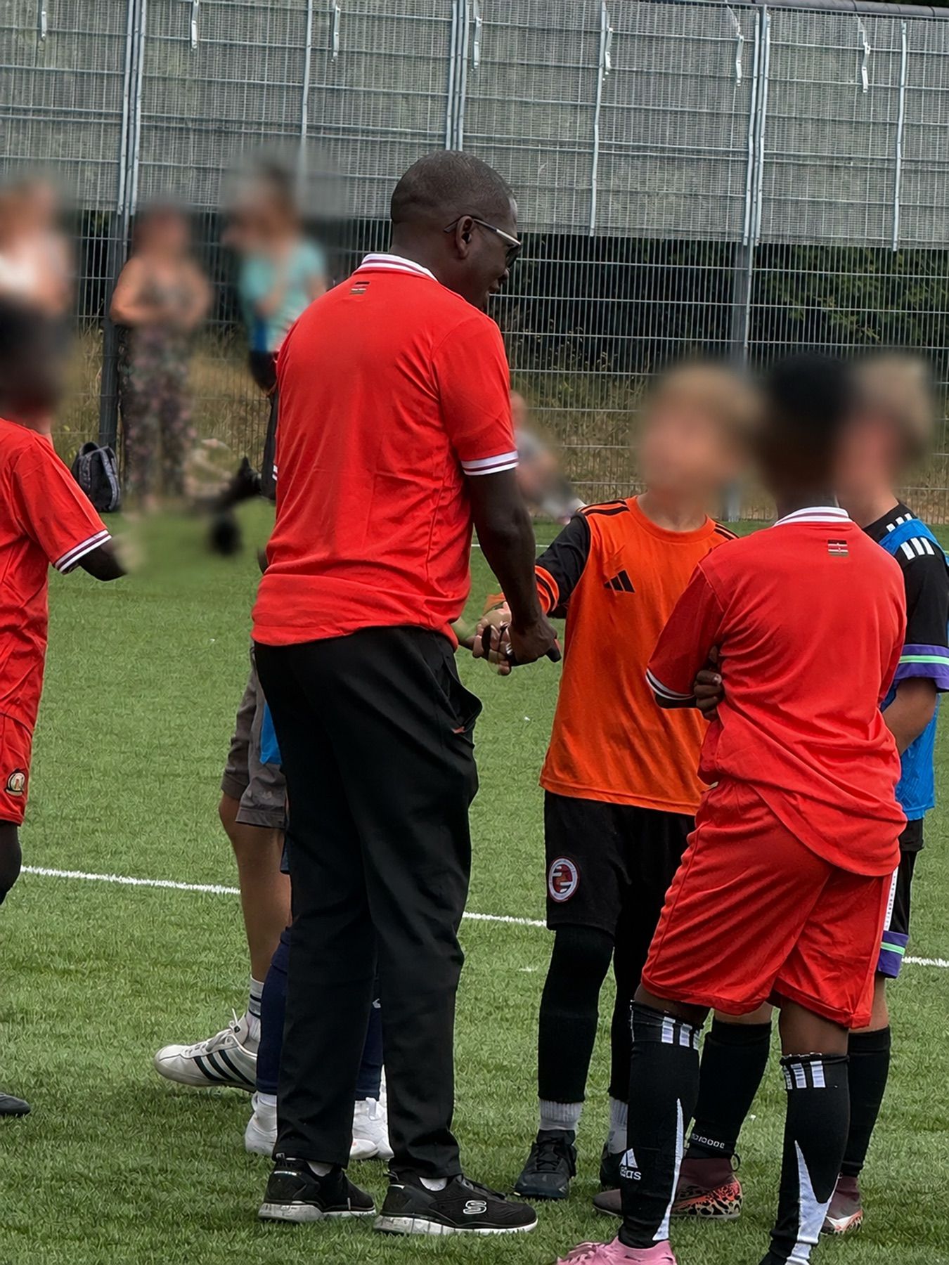 A coach greeting young football players on the pitch