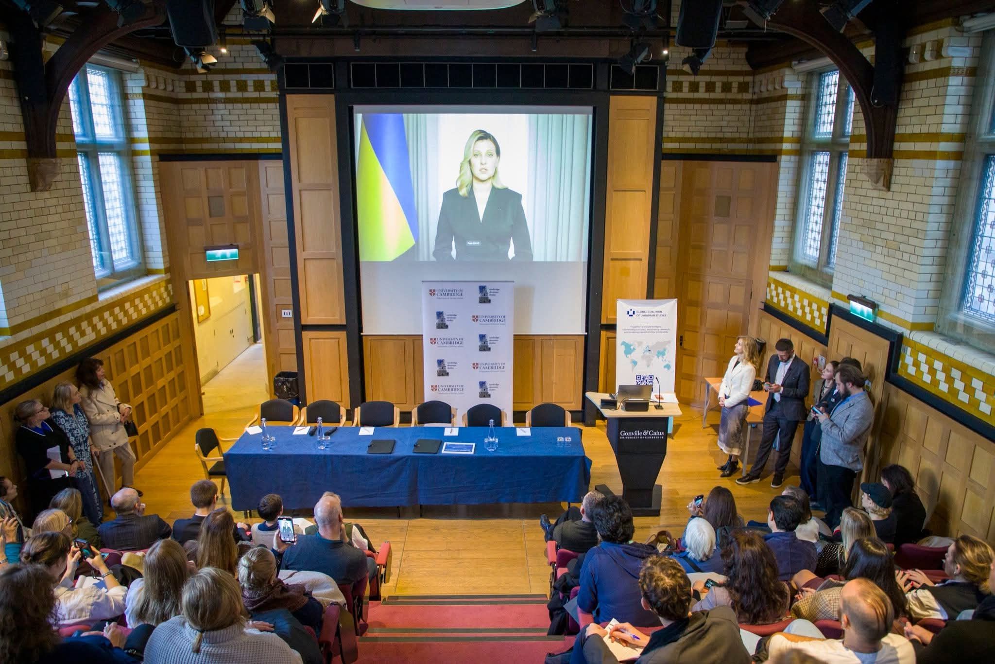 Audience in a panelled hall at Gonville & Caius watching a video address at the memorandum signing