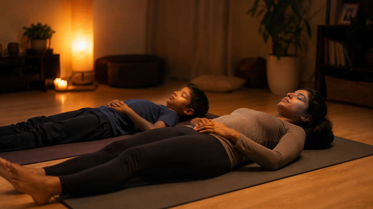 A parent and child lying side by side on yoga mats practising body scan meditation together at home