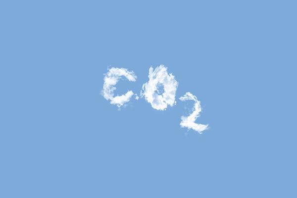 White clouds in the shape of CO2 letters against a clear blue sky, symbolizing carbon emissions and environmental impact.