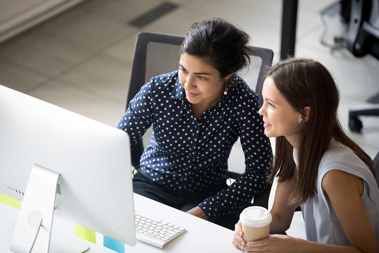 Image of two people at a desk looking at a computer.