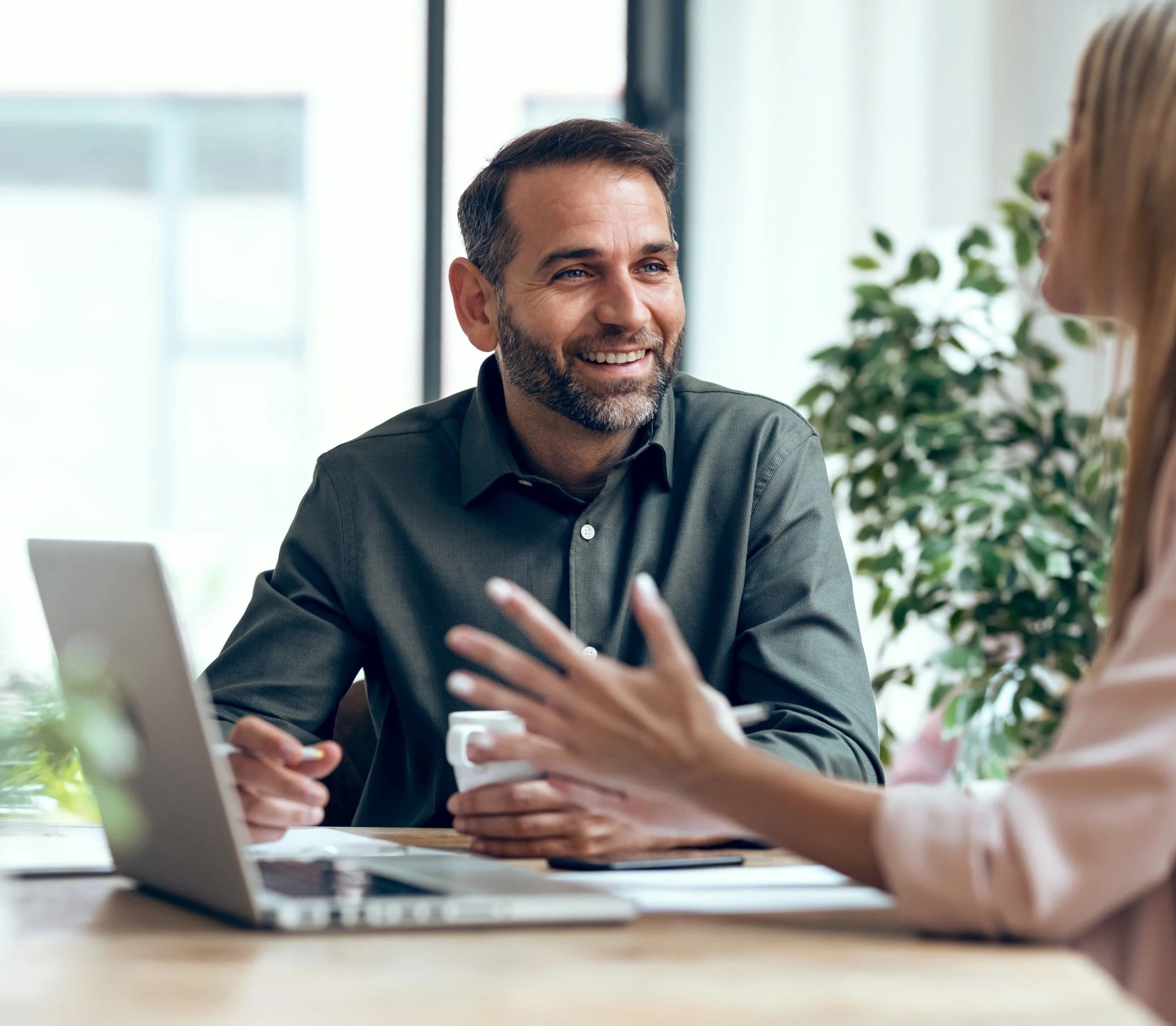 Photo of a person talking to another person in front of a laptop at an office.