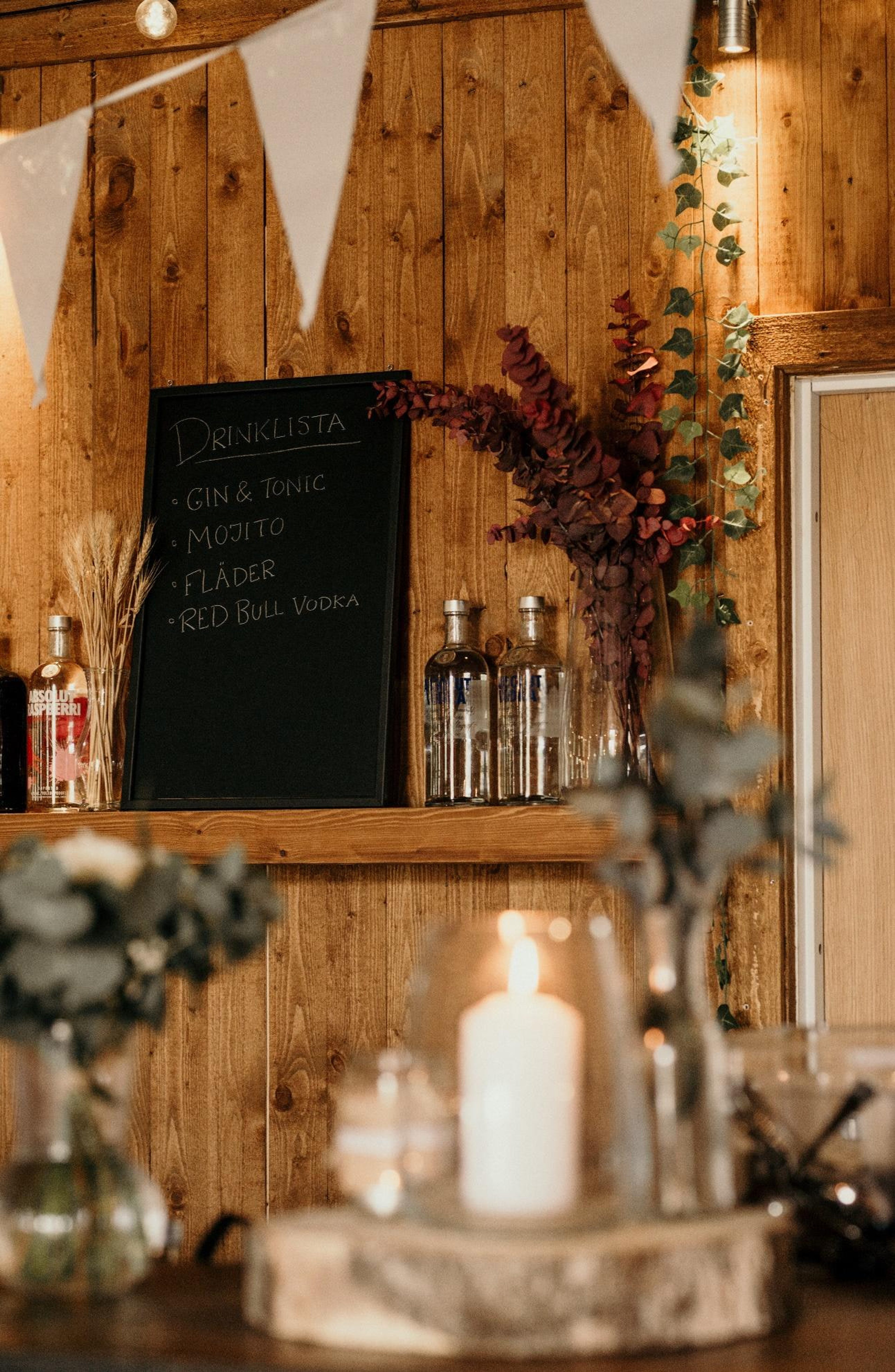 Handskriven drinklista på svart tavla vid baren, med grönska och levande ljus