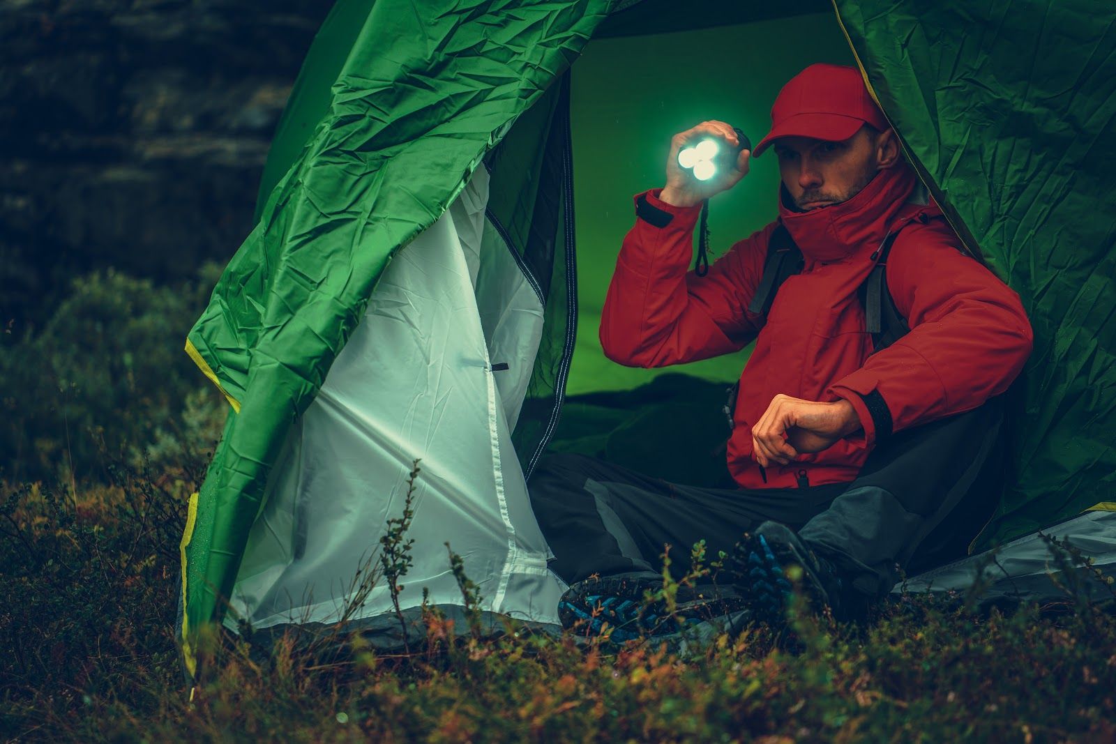 Caucasian Camper with Flashlight Inside His Tent During Rainy Evening While on Hike.