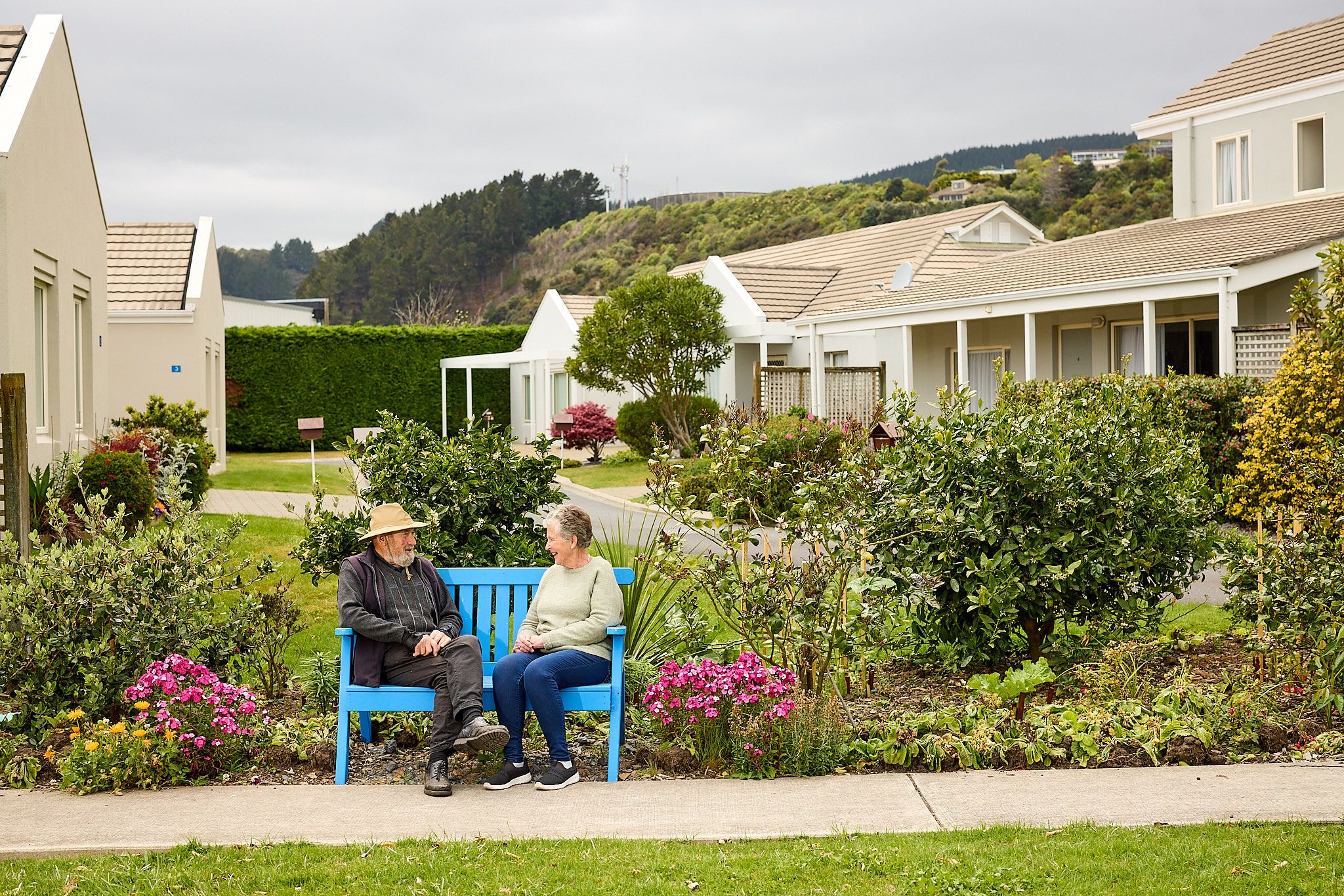 Two residents sitting down on a park bench outside Coastal Villas