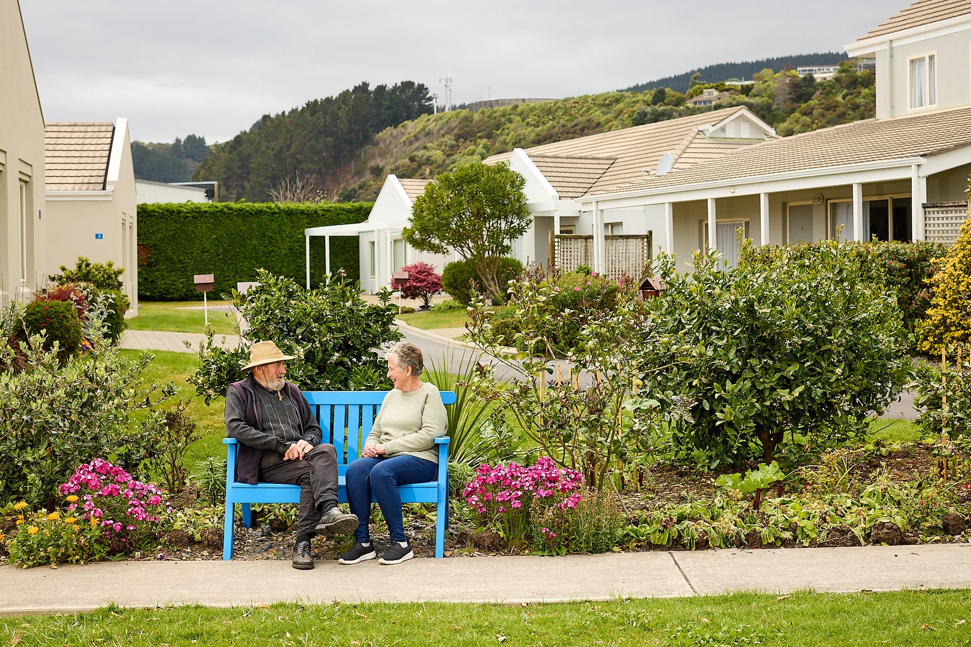 Two residents sitting down on a park bench outside Coastal Villas