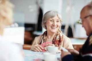 Elderly woman smiling while playing cards with a group of peers