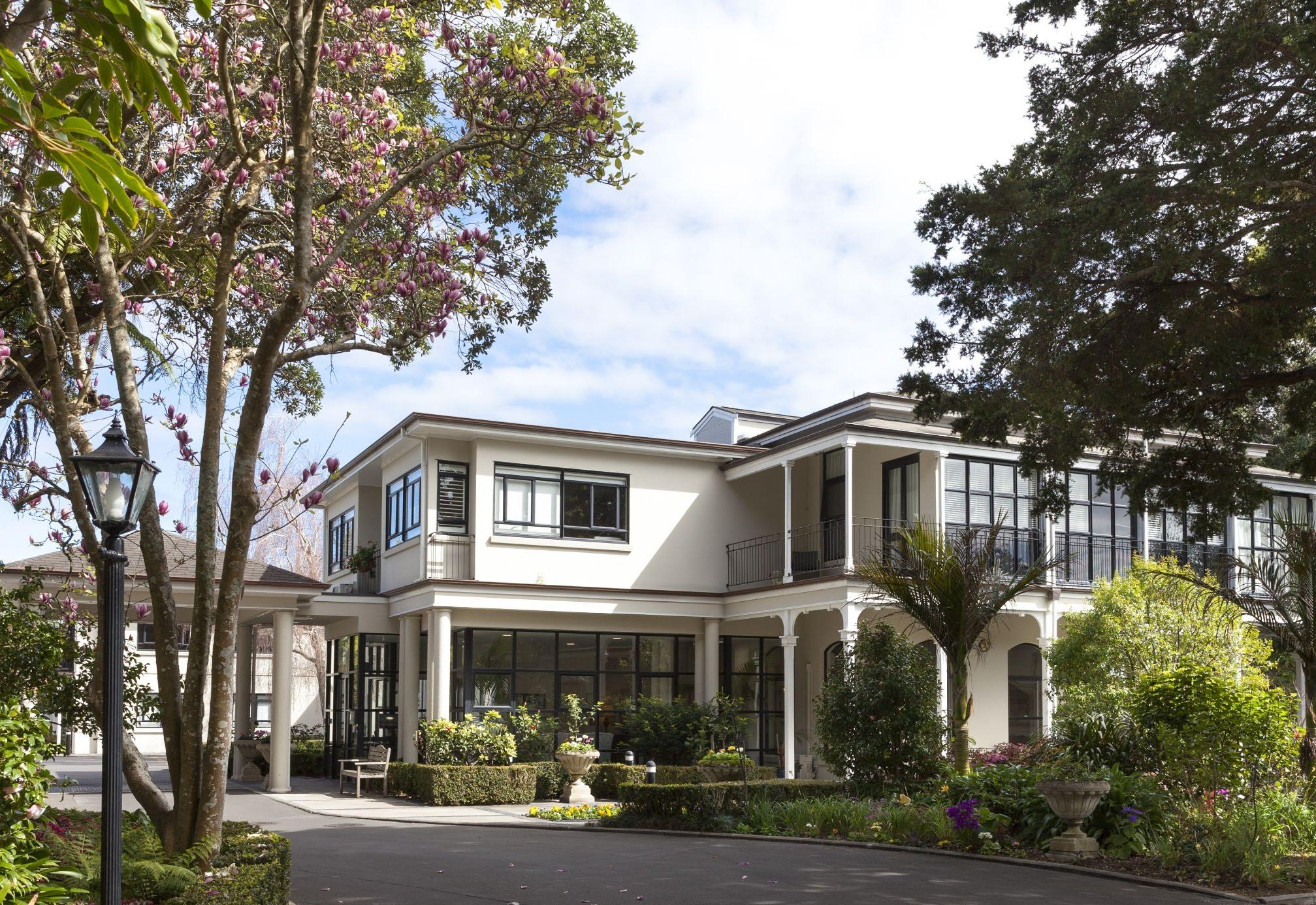 A large white house surrounded by lush trees at Metlifecare's Remuera retirement village.