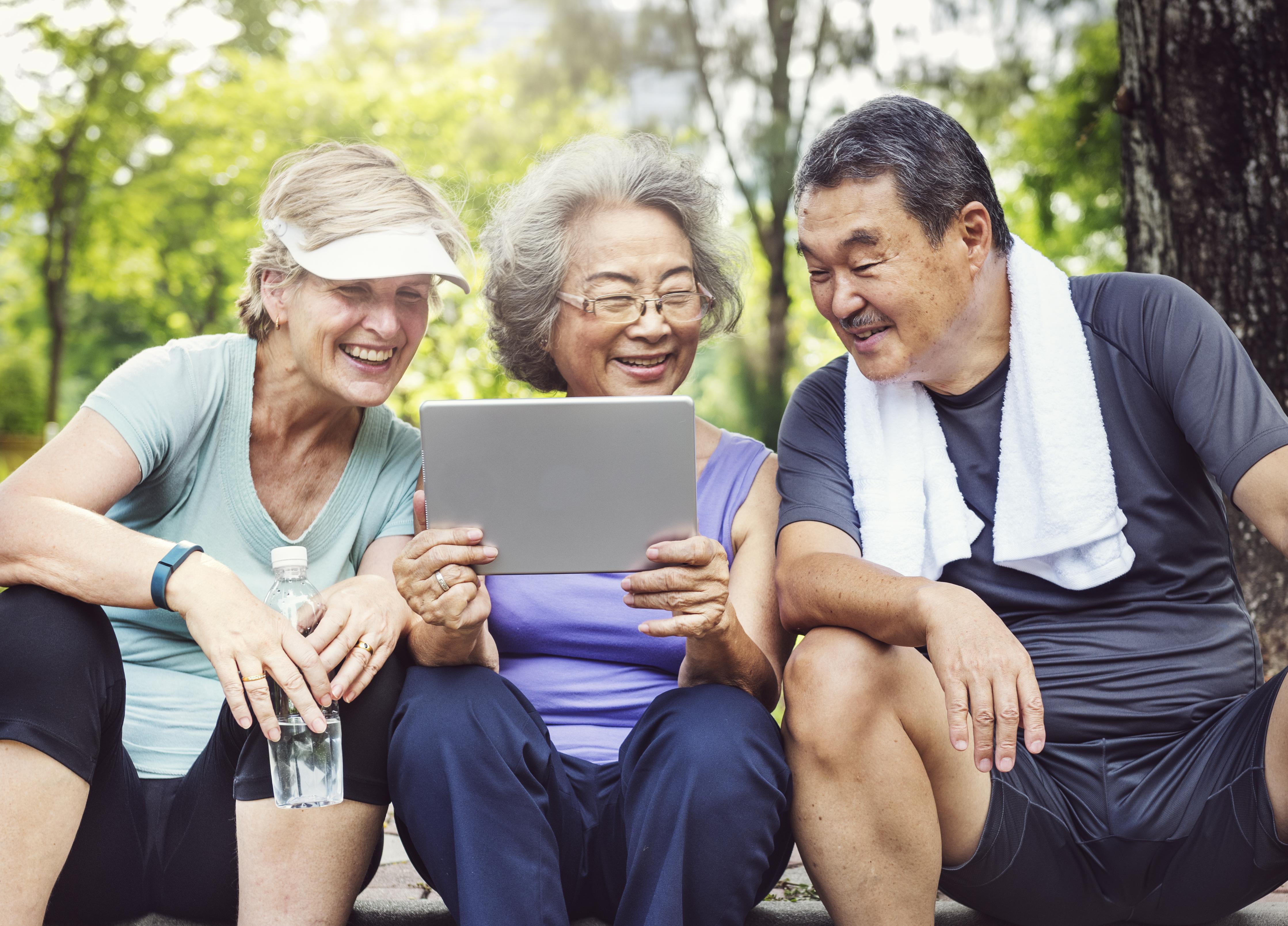 Three elderly smiling as they gather around a tablet.