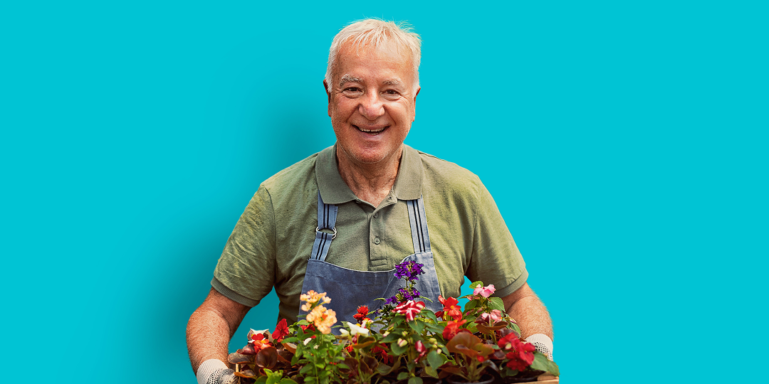 Smiling retirement village resident holding flowers in a community garden during a national open day at a New Zealand retirement village.