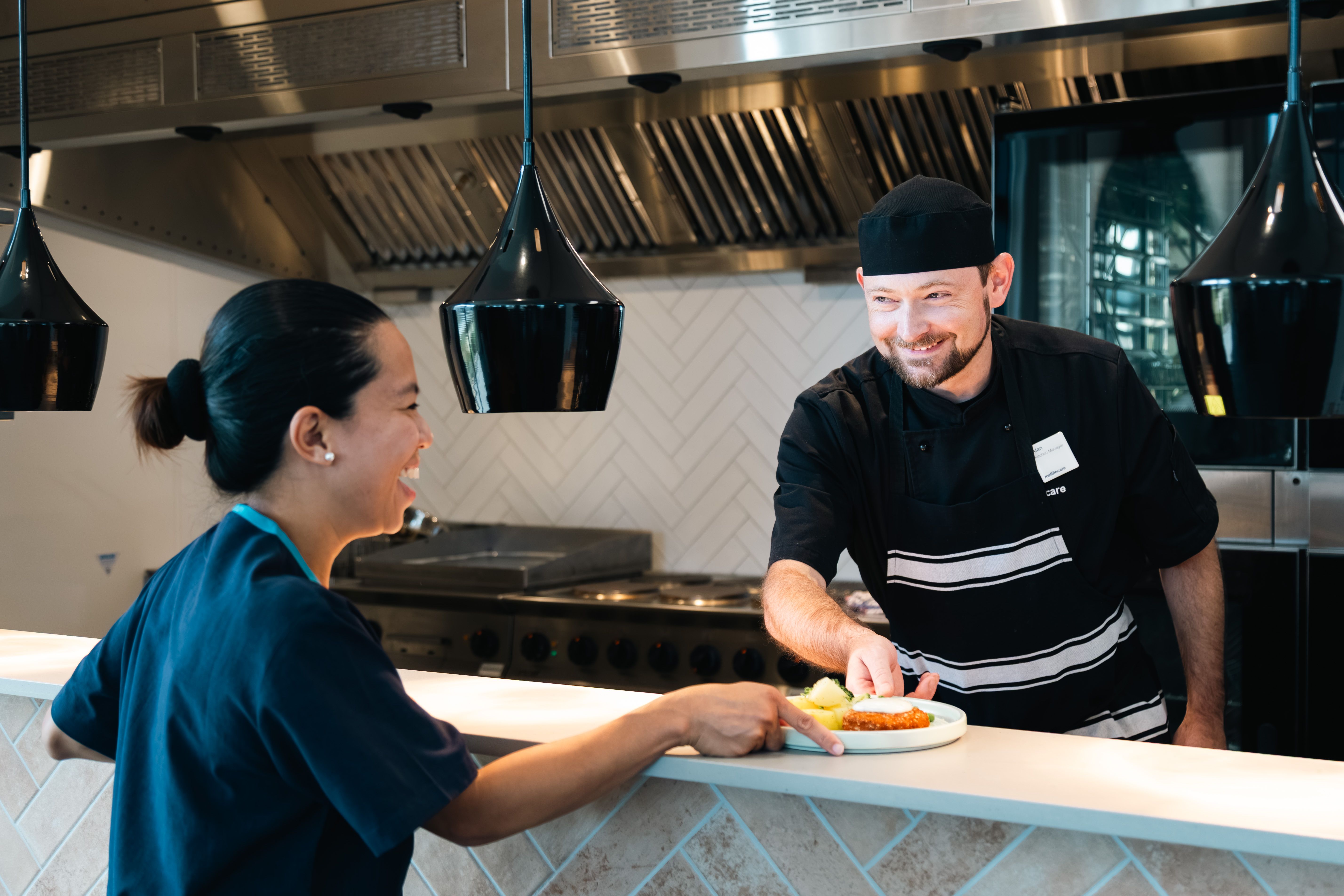 Ched handing a plated meal to a nurse smiling