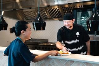 Ched handing a plated meal to a nurse smiling