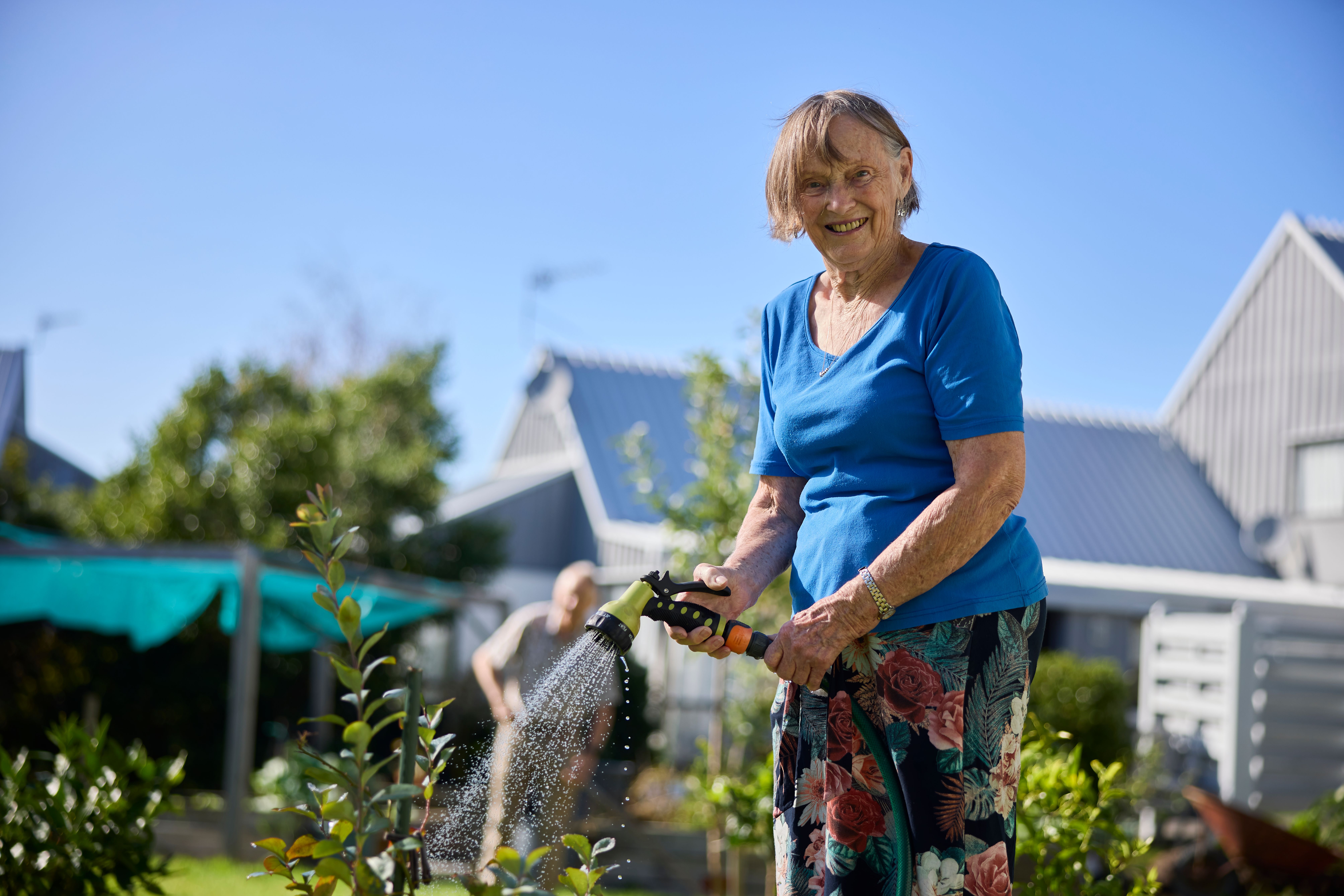 Resident watering her garden outside with blue top on