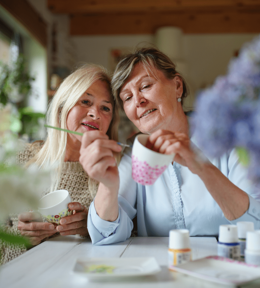 Two women painting mugs together, symbolising friendship and retirement village living.