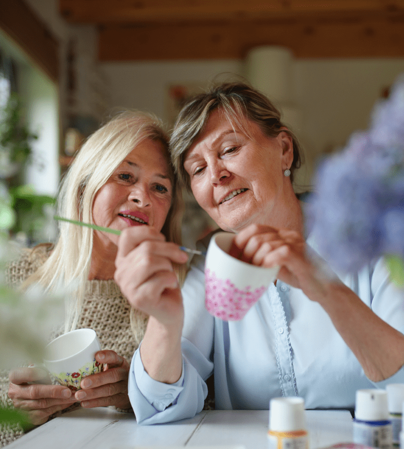 Two women painting mugs together, symbolising friendship and retirement village living.