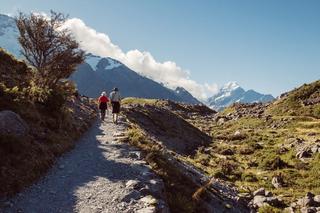 Two people sitting walking along lake and mountains