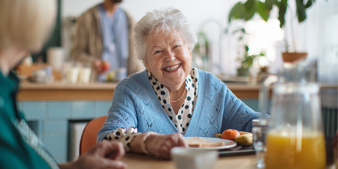 Smiling resident enjoying a welcoming meal in a retirement village care home during an open weekend.