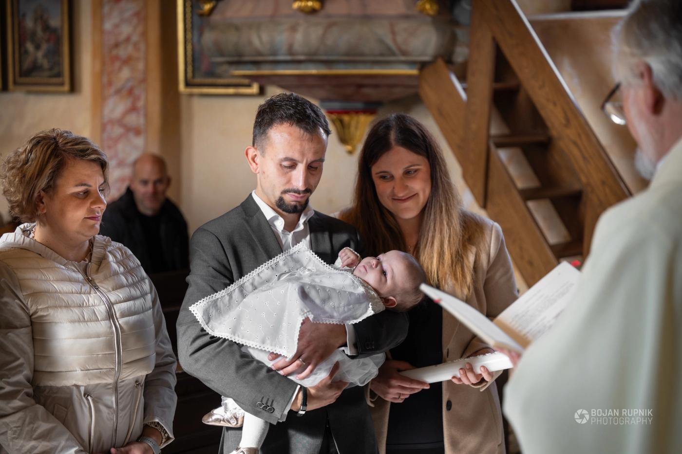 Starša držita dojenčka v krstni obleki med krstom v cerkvi