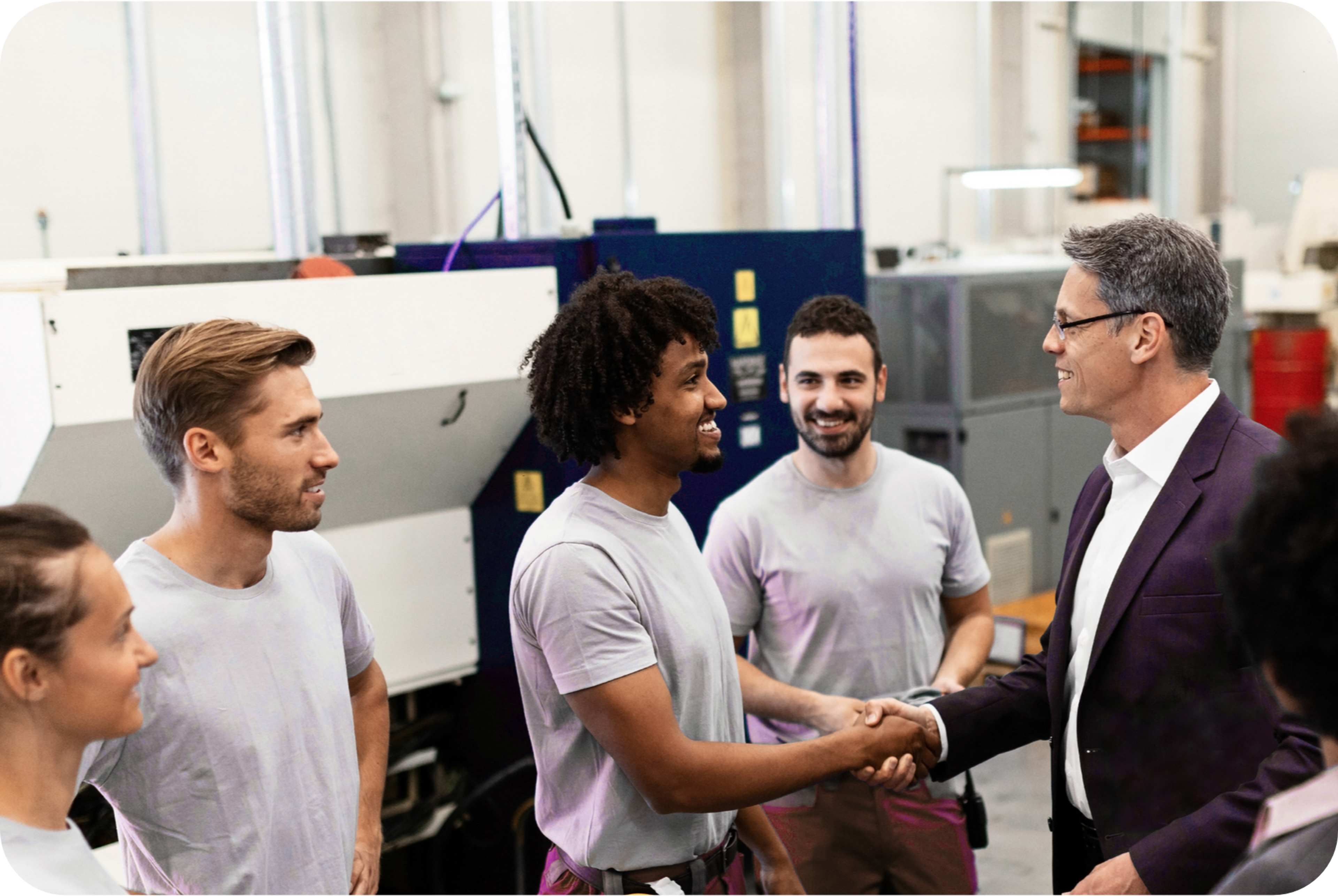 Picture of a middle aged business man shaking hands with an African worker wearing a white t-shirt, while a Caucasian worker with a black beard watches them