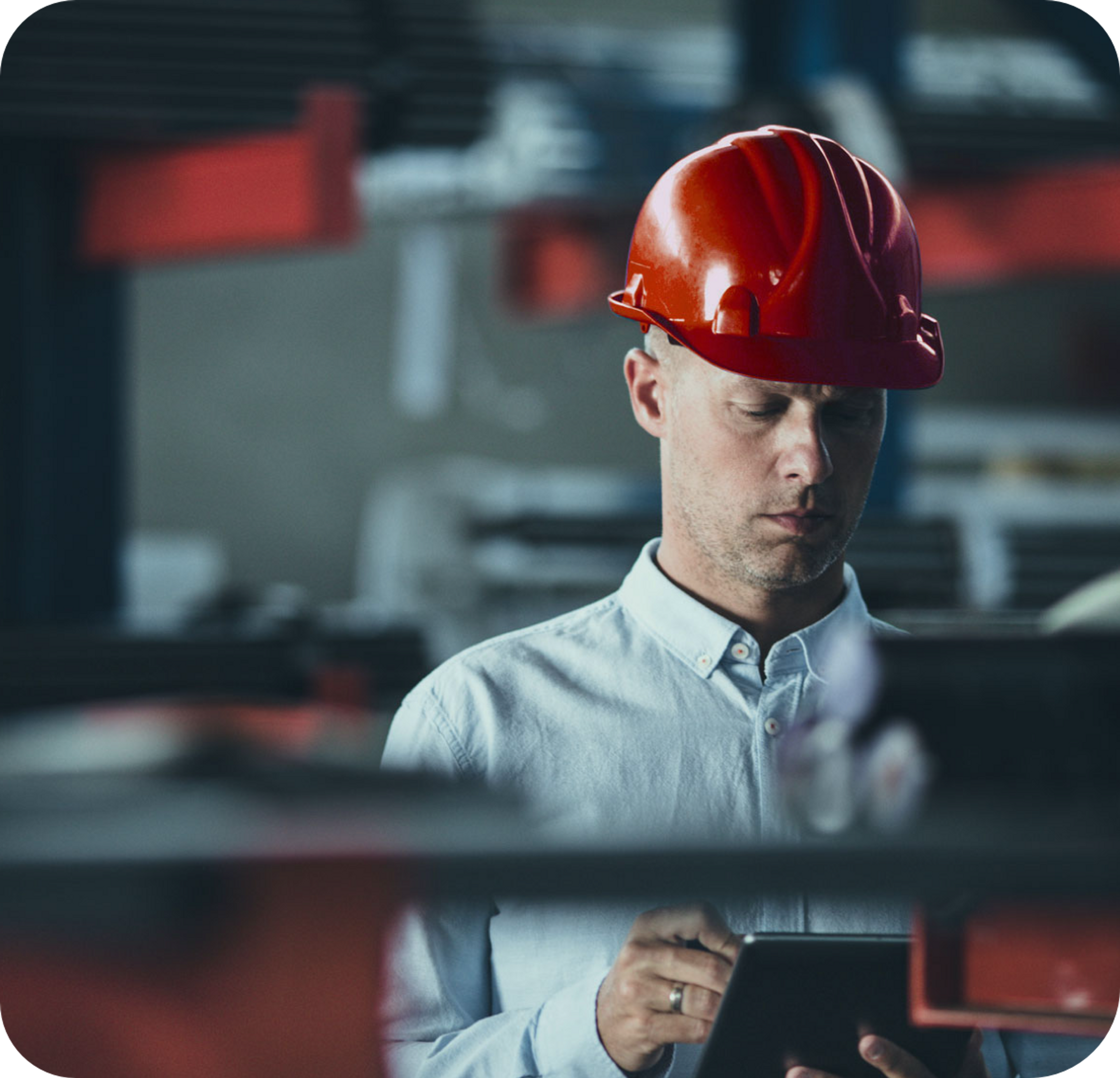 Picture of Caucasian male wearing red hard hat, bllue collared shirt and wearing silver wedding ring , operating an ipad using a stylus in a warehouse setting