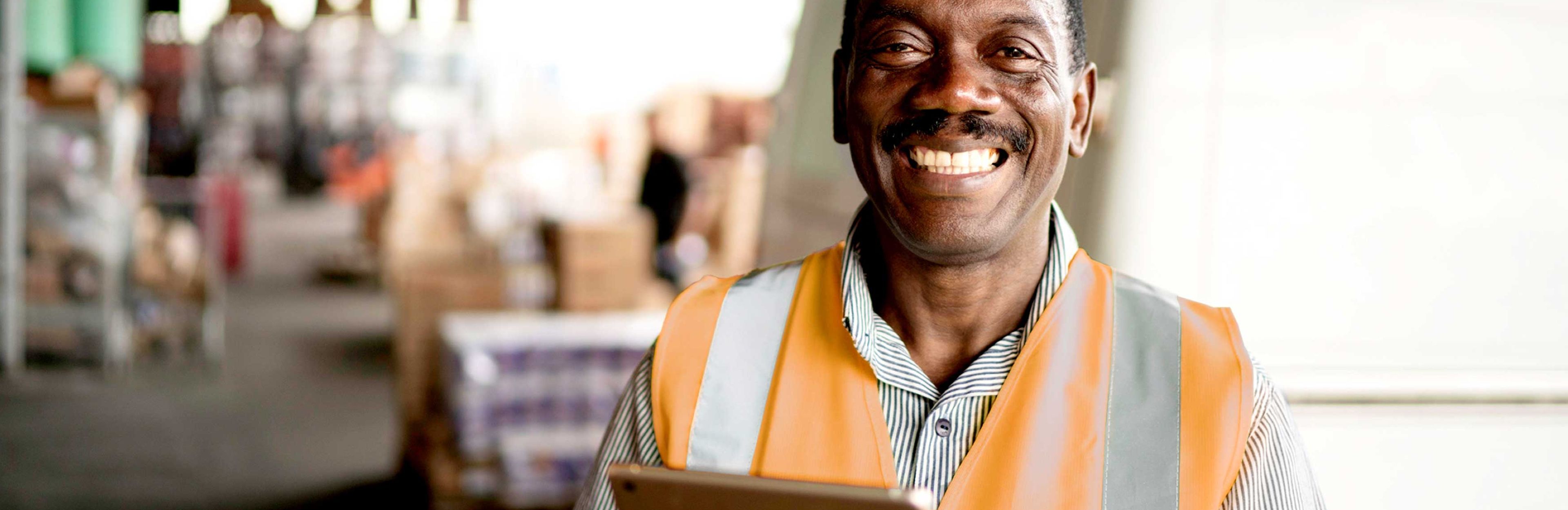 Picture of African man smiling wearing orange safety vest and holding an iPad