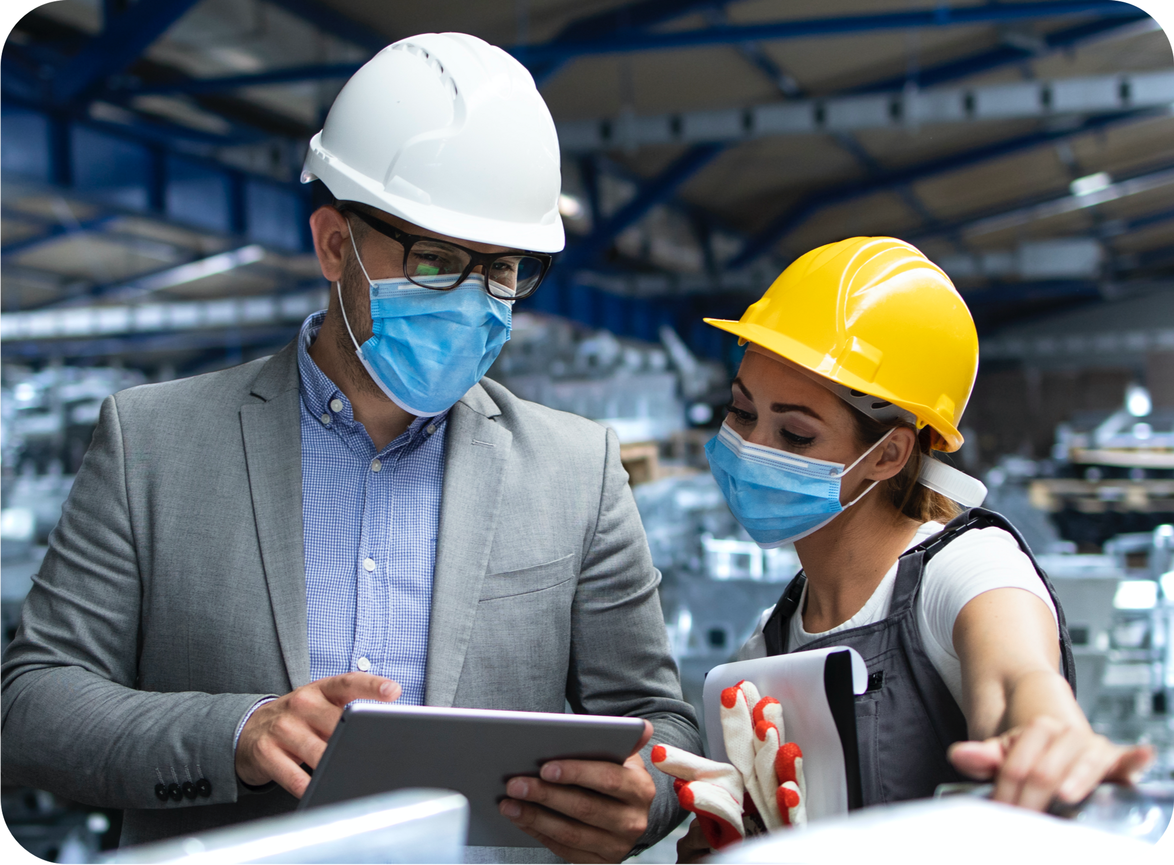 Picture of Caucasian Man in a warehouse setting wearing white hard hat and blue surgical mask and gray suit jacket and blue collared shrirt talks to an ethnic woman wearing jean coveralls, white tshirt and yellow hard hat the contents shown in his Ipad