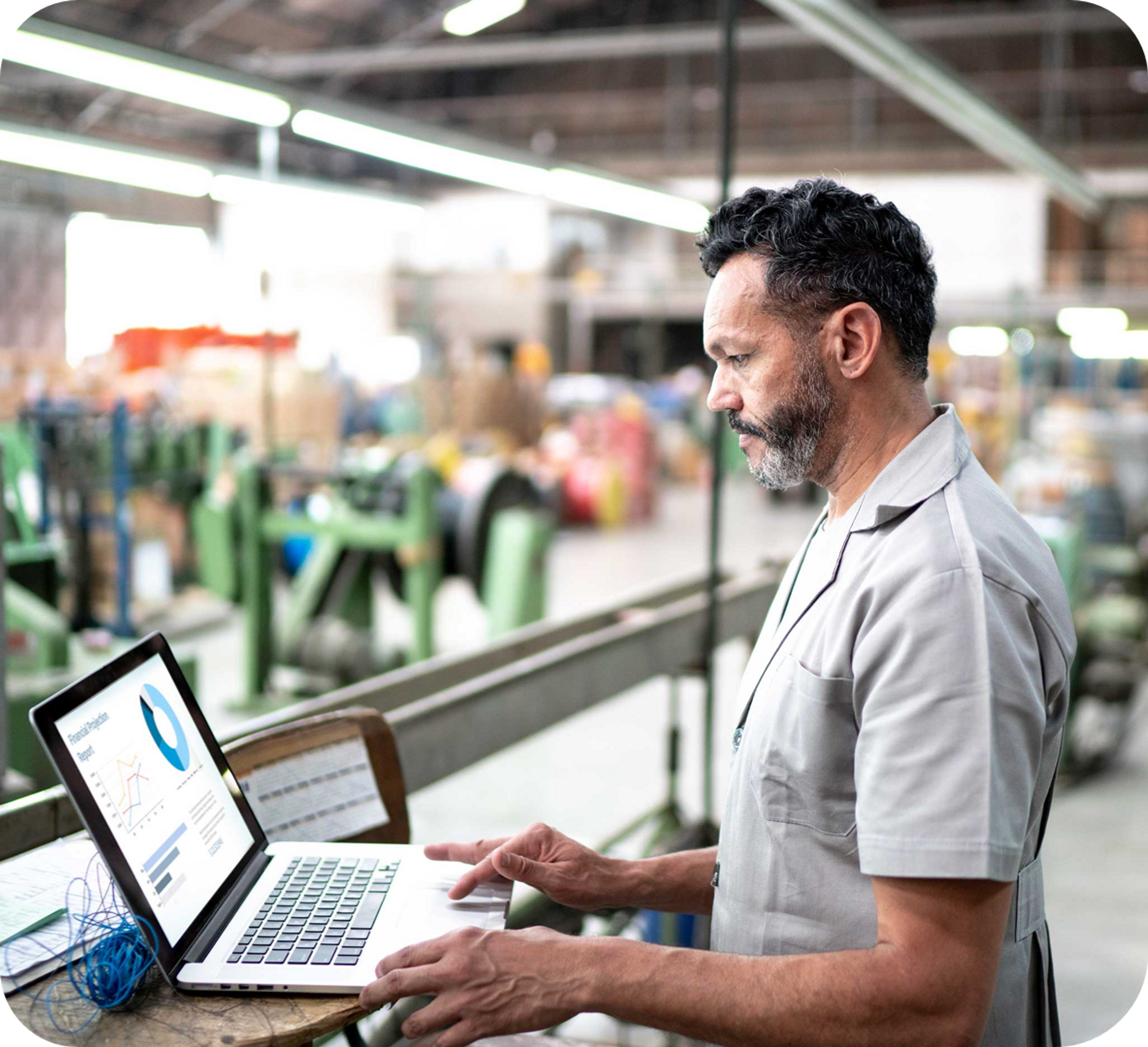 Picture of middle aged man with back and silver beard and white dress shirt using a laptop in a warehouse