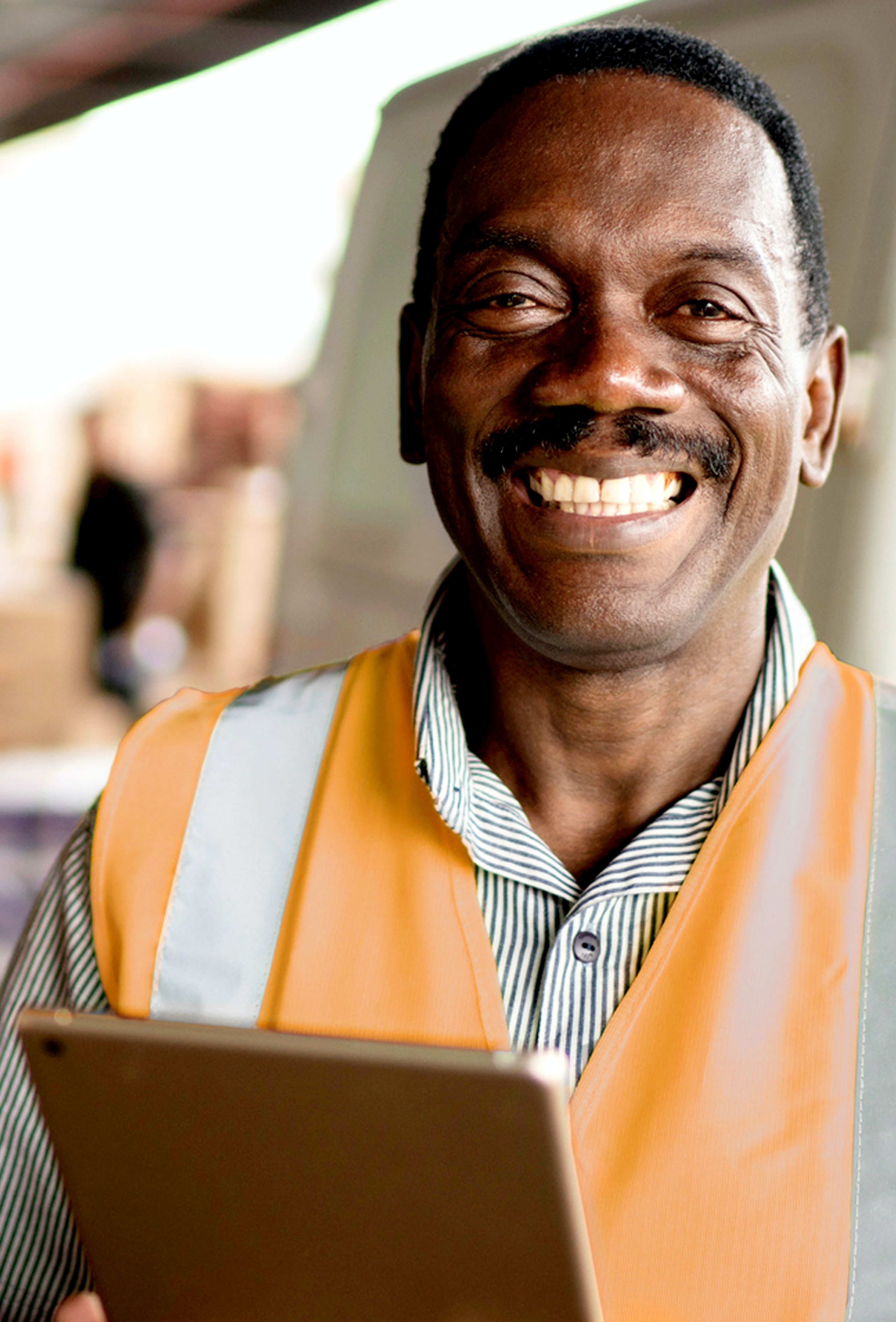  Photo d'un homme africain souriant portant un gilet de sécurité orange et tenant un ipad