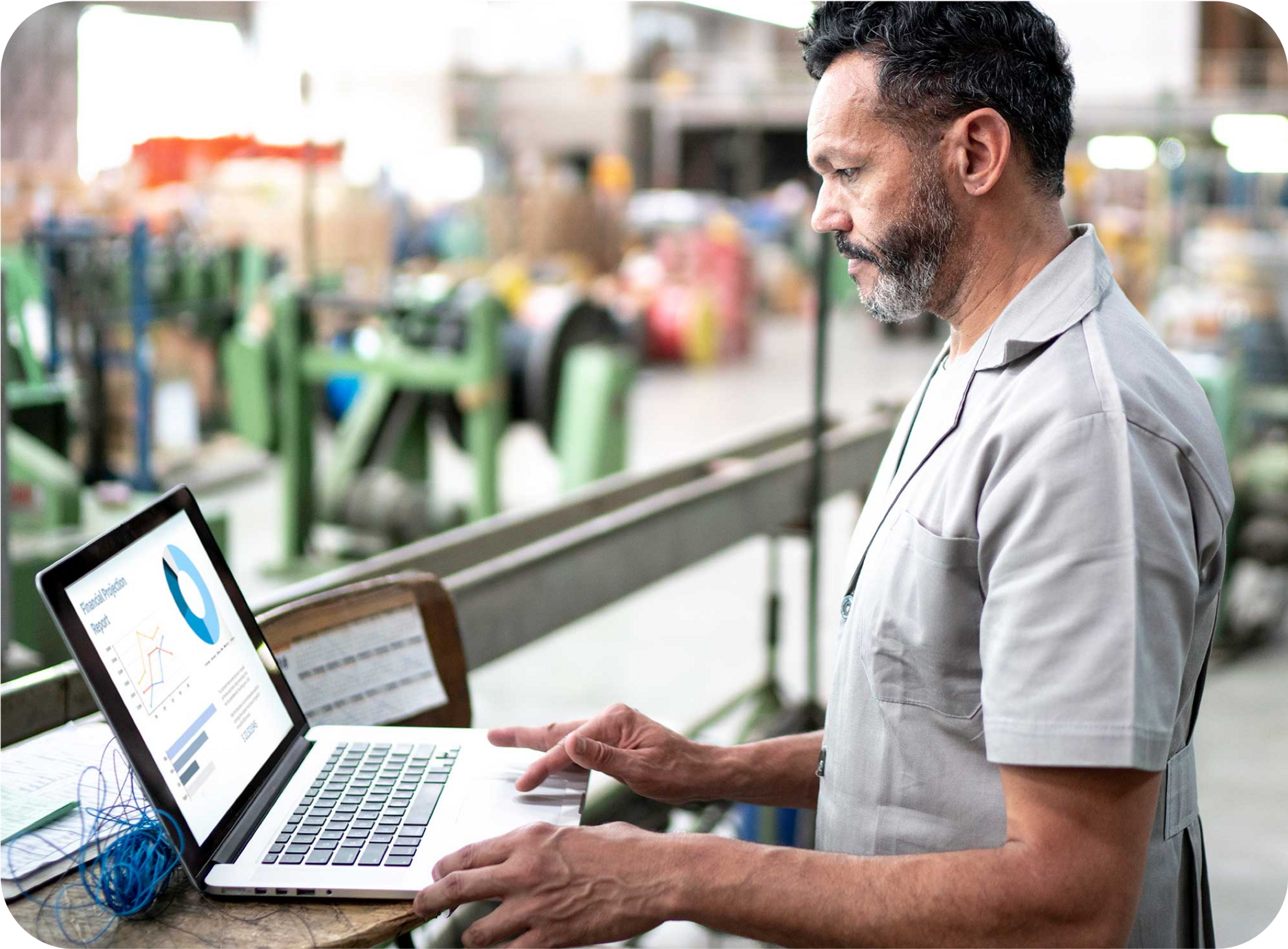 Photo d'un homme d'âge moyen avec barbe grisonnante et chemise blanche devant un ordinateur portable dans un entrepôt