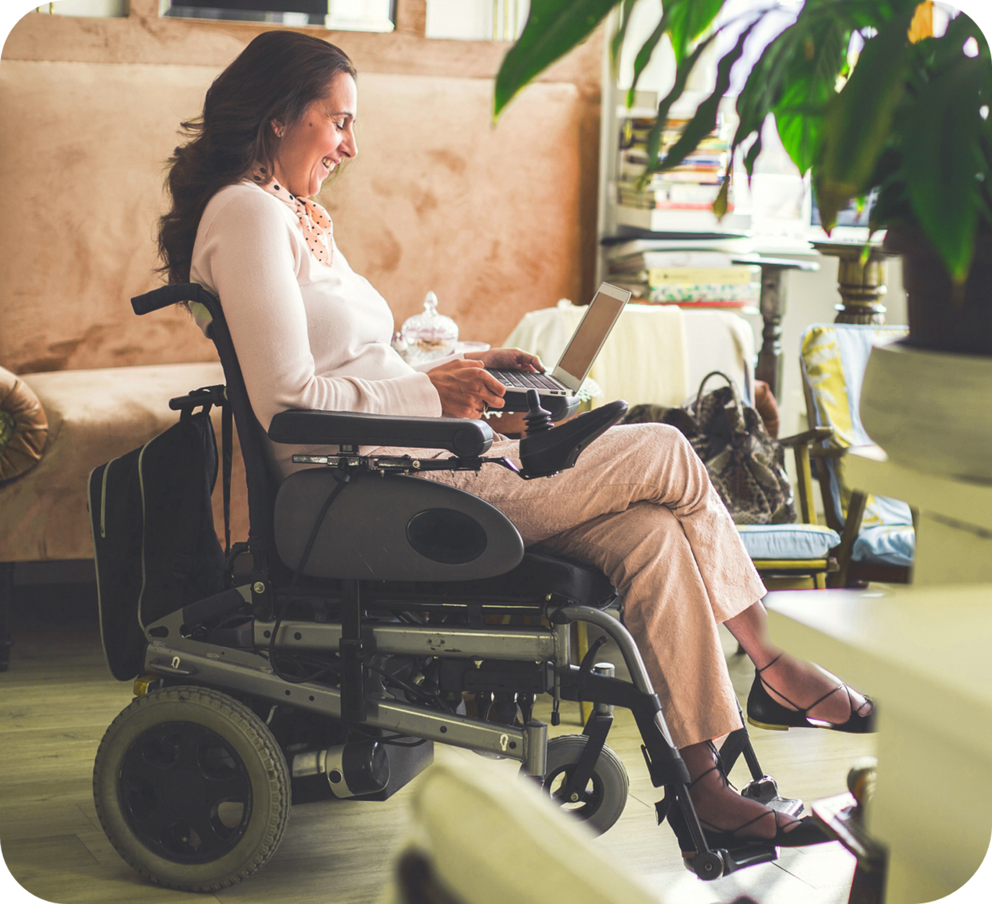 Photo of smiling Caucasian woman sitting on a motorized wheelchair and using her laptop
