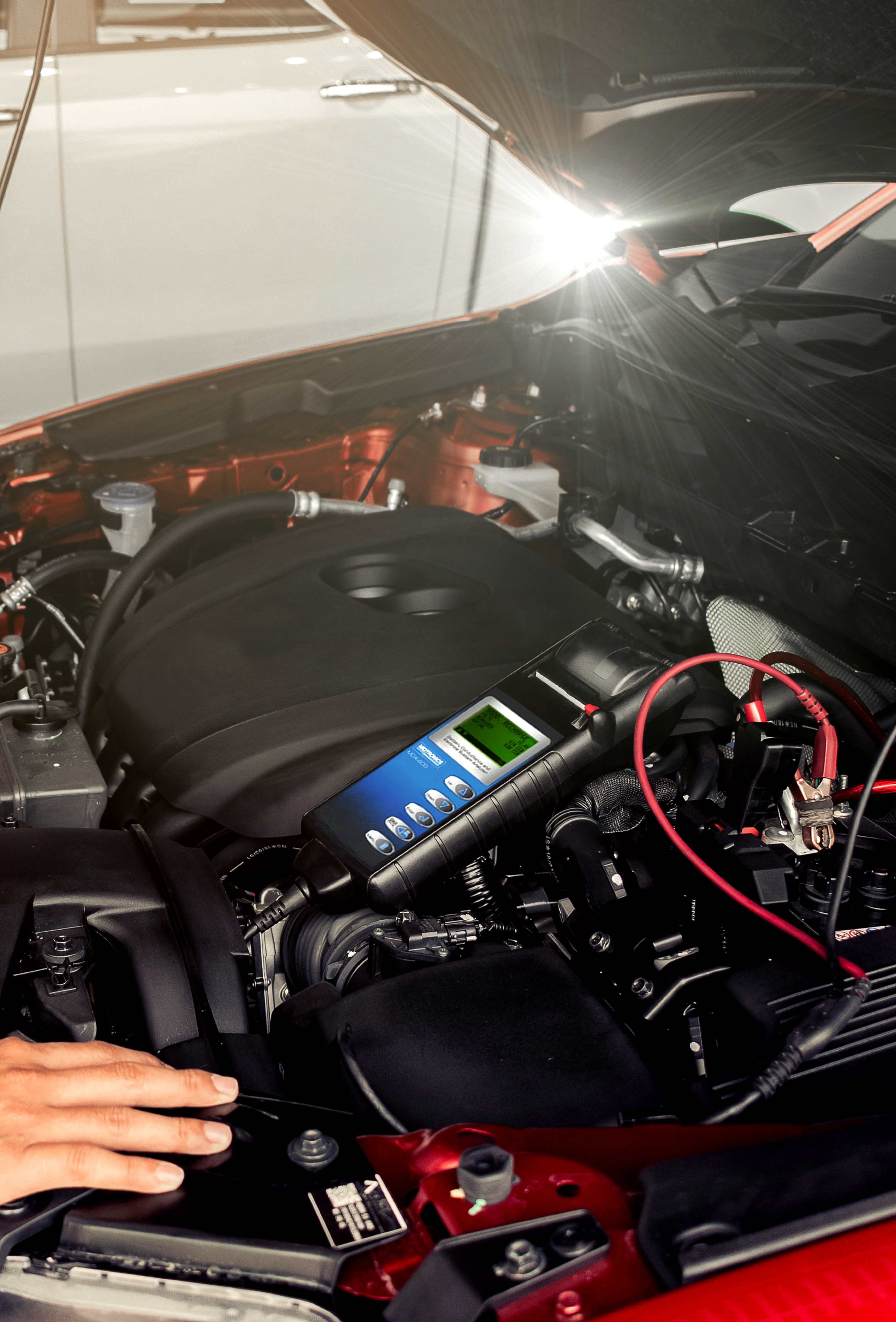 Picture of man holding his hand to a car battery inside the open hood of a car