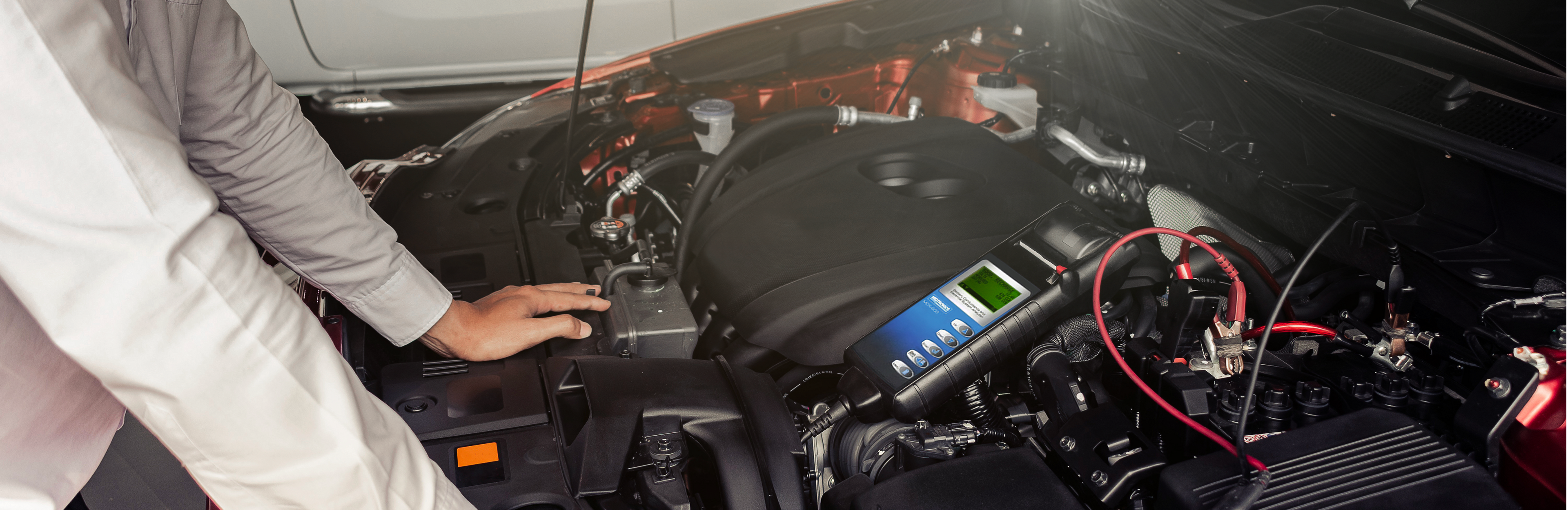 Picture of man holding his hand to a car battery inside the open hood of a car