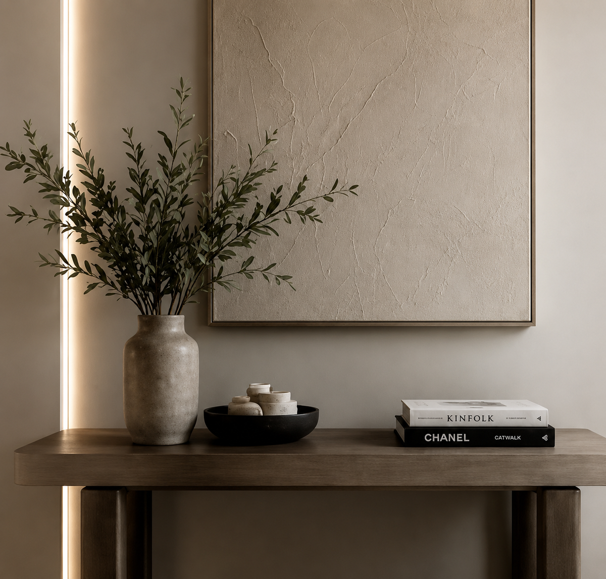 Neutral console table styled with branching greenery, a textured wall artwork and curated decor